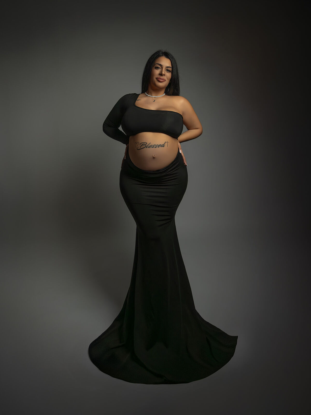 Mujer embarazada posando con vestido largo negro y vientre tatuado en estudio profesional, durante una sesión de embarazo elegante en Cartagena por Torres & Torres Fotografía