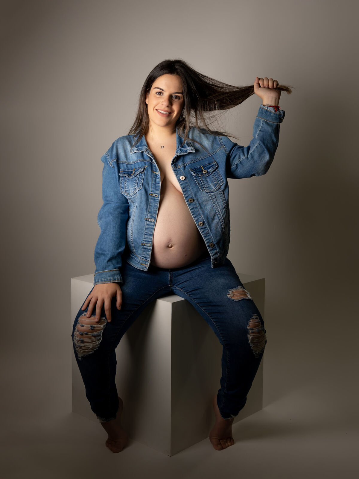 Retrato de embarazo con chaqueta y pantalones vaqueros rasgados en estudio profesional en Cartagena por Torres & Torres Fotografía