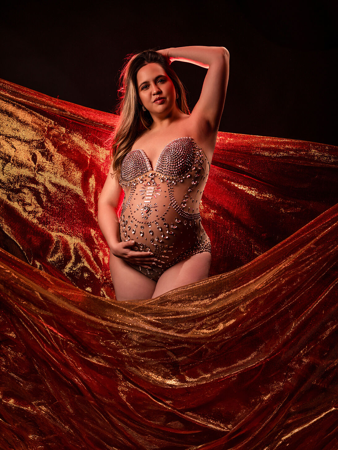 Retrato de embarazo glamurosa con bodysuit de pedrería y tela dorada de fondo en estudio en Cartagena por Torres & Torres Fotografía