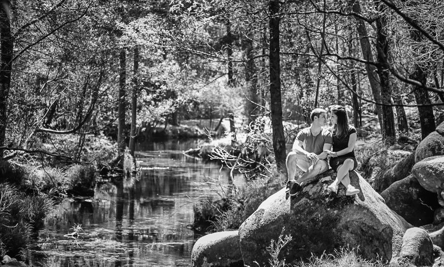 Casal de namorados sentados numa pedra a beira de um lago
