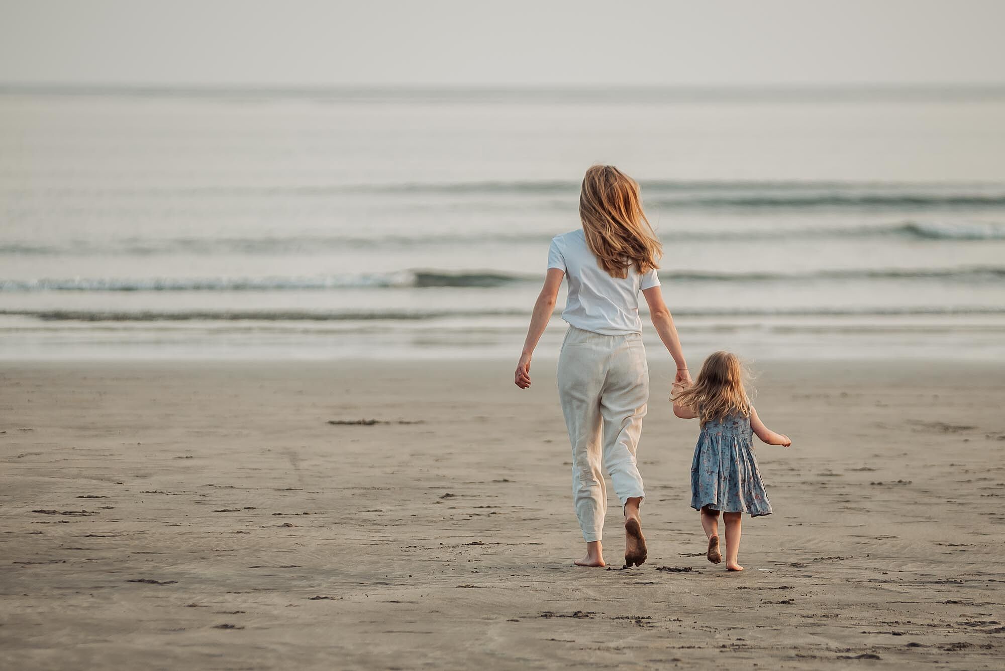 mae-e-filha-de-maos-dadas-na-praia-ao-por-do-sol