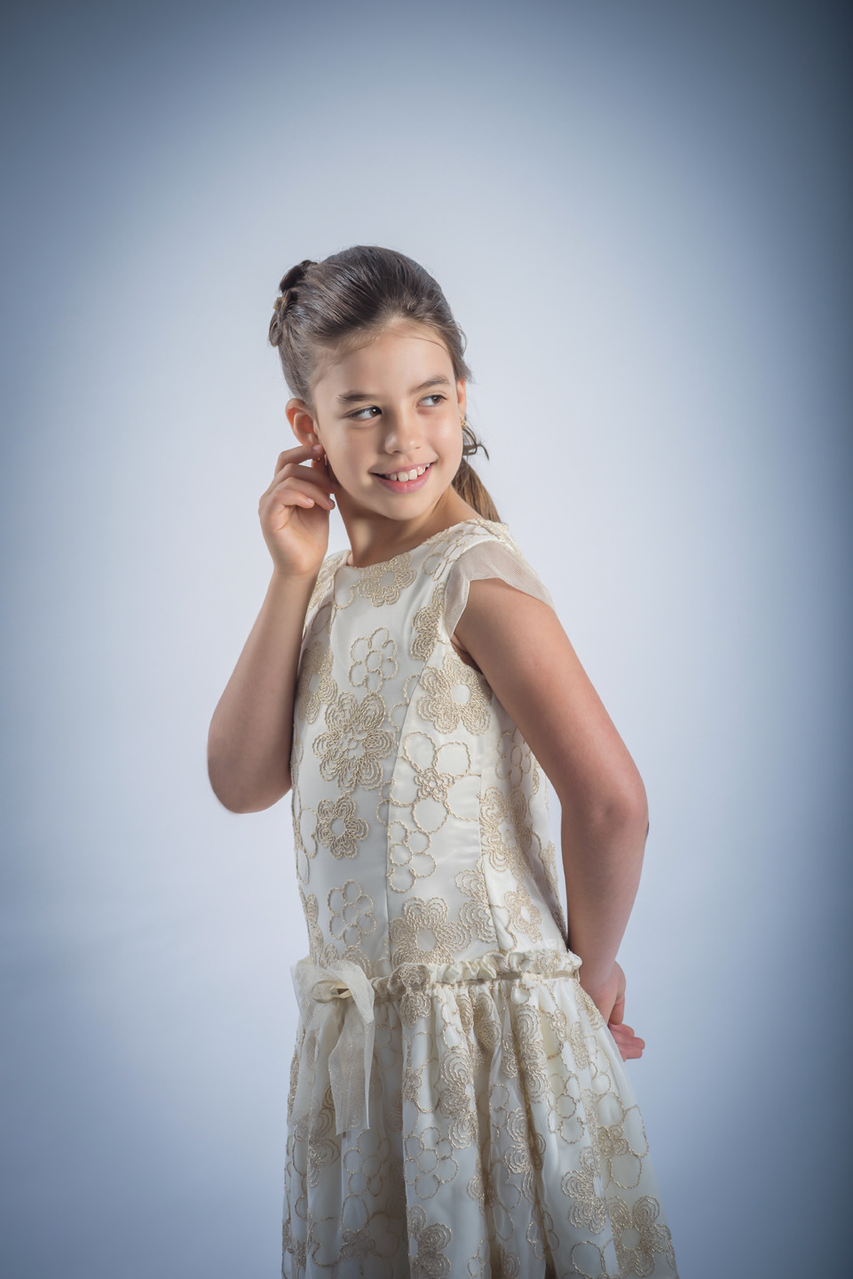 Menina de vestido com a mão no canto da orelha a olhar para o lado e a sorrir