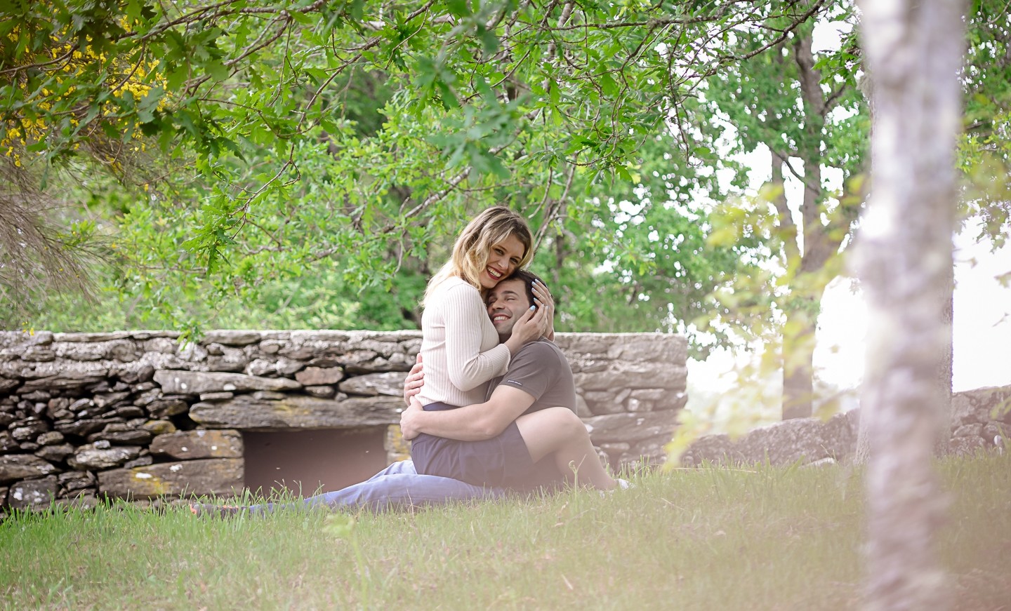 Casal de namorados a darem um abra&ccedil;o enquanto est&atilde;o sentados na relva 