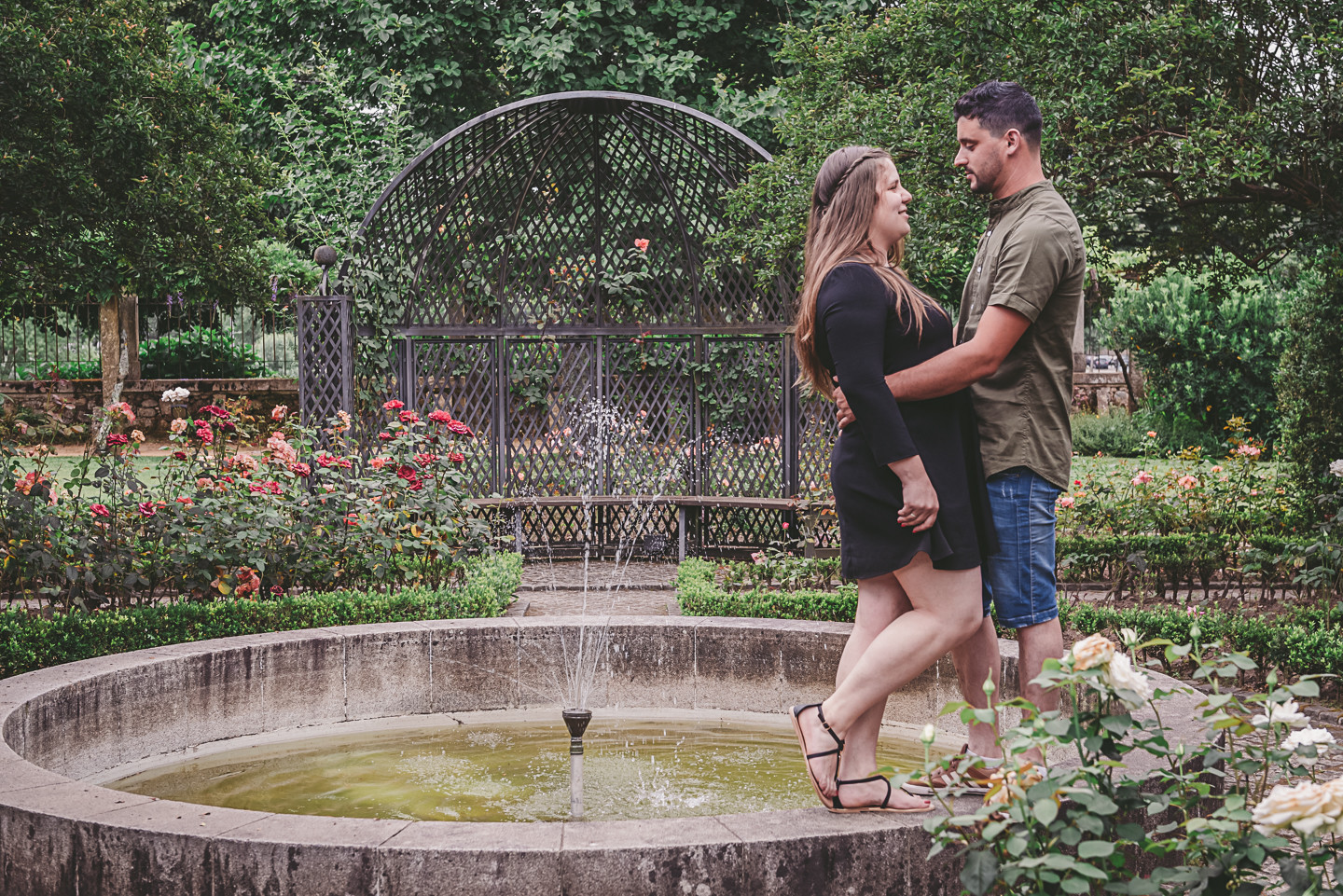 Casal de namorados em cima do muro da fonte em quanto o homem segura a namorada pela a cintura