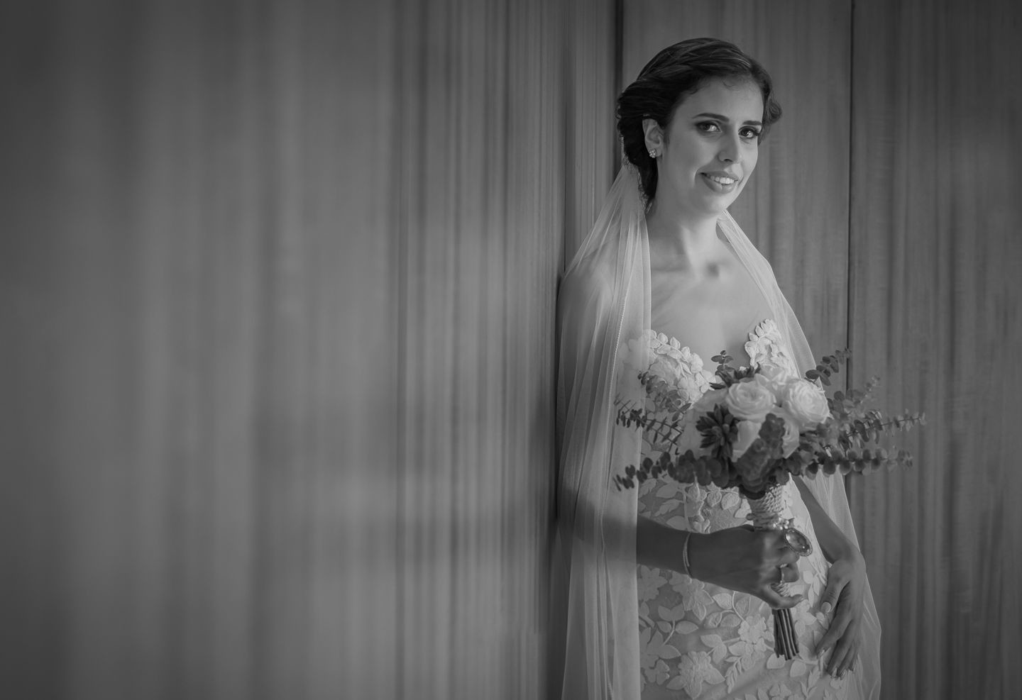A noiva encostada a parede a fazer pose e com o buque de flores