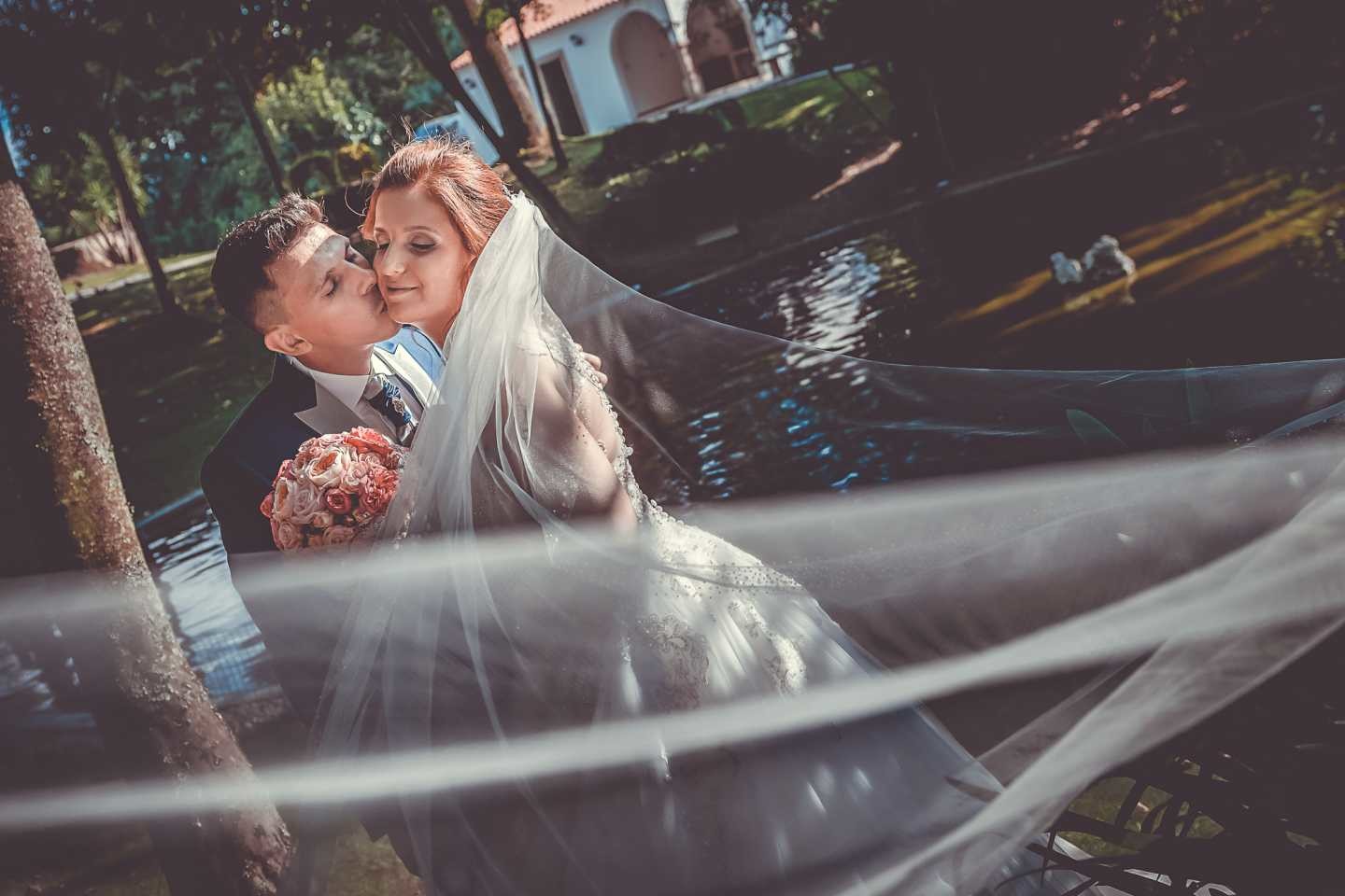 Noivo a dar um beijo na bochecha da noiva a beira do lago