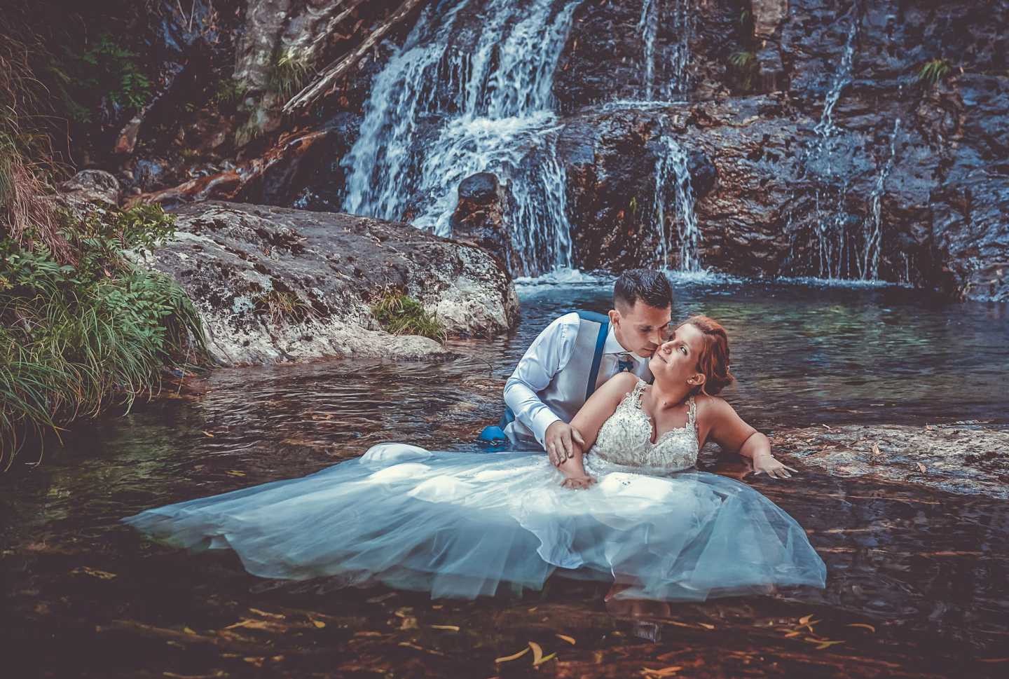 Noiva sentada dentro do lago enquanto o noivo lhe segura