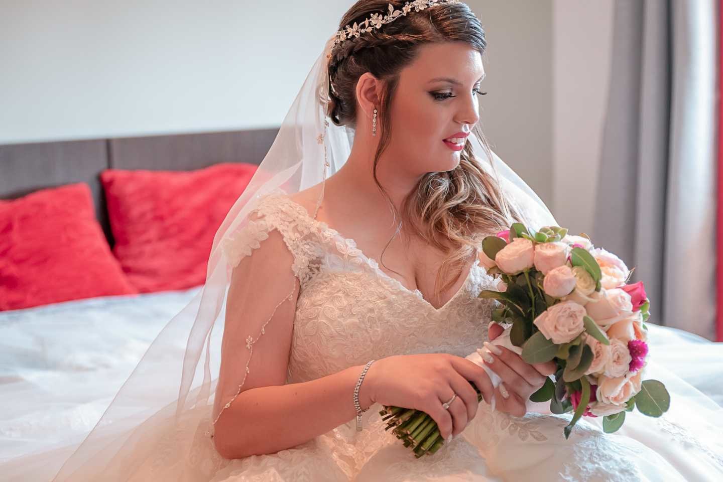 Noiva sentada na cama a segurar o buque de flores