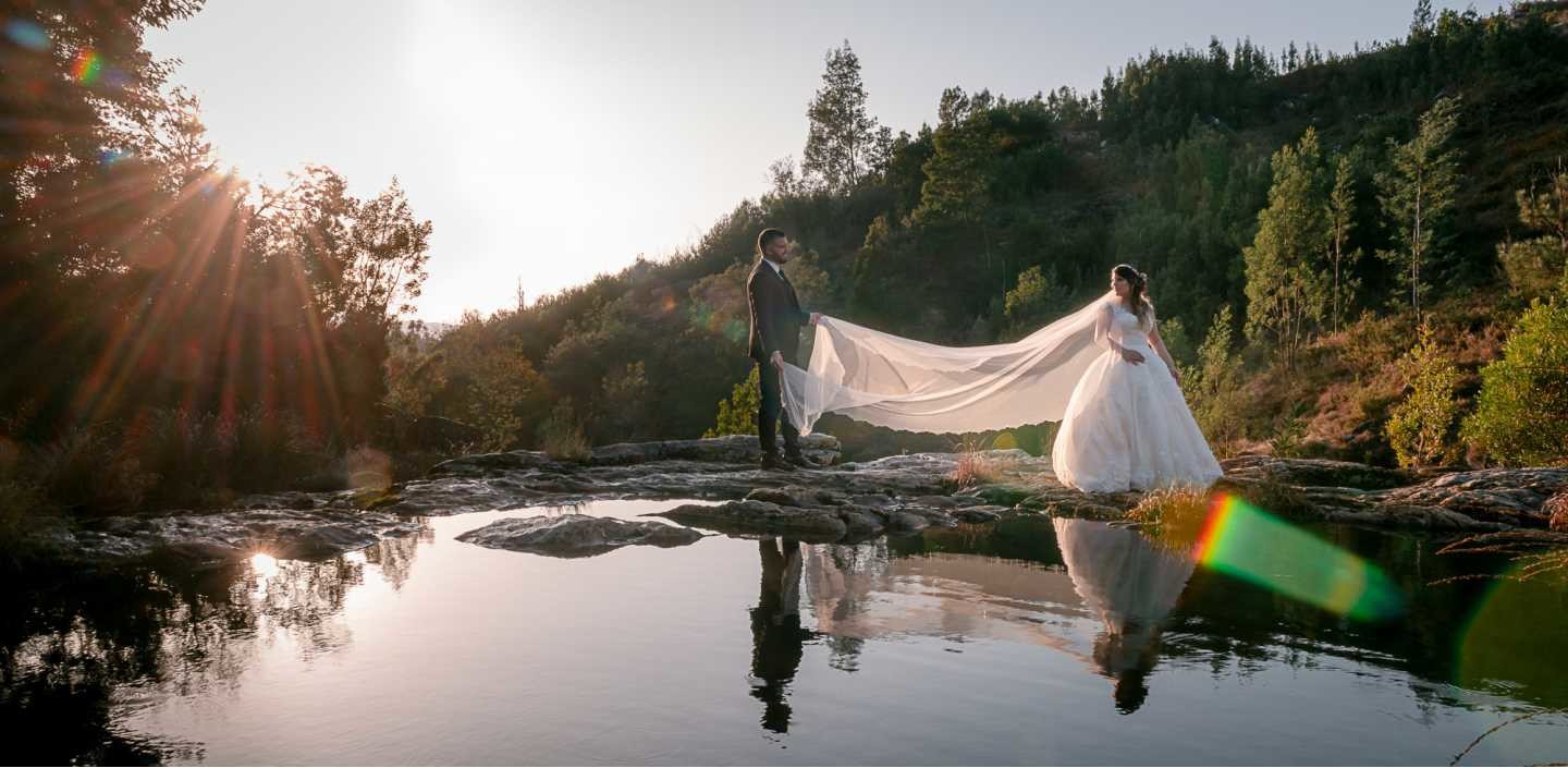 Noivo a segurar no véu da noiva a beira do lago