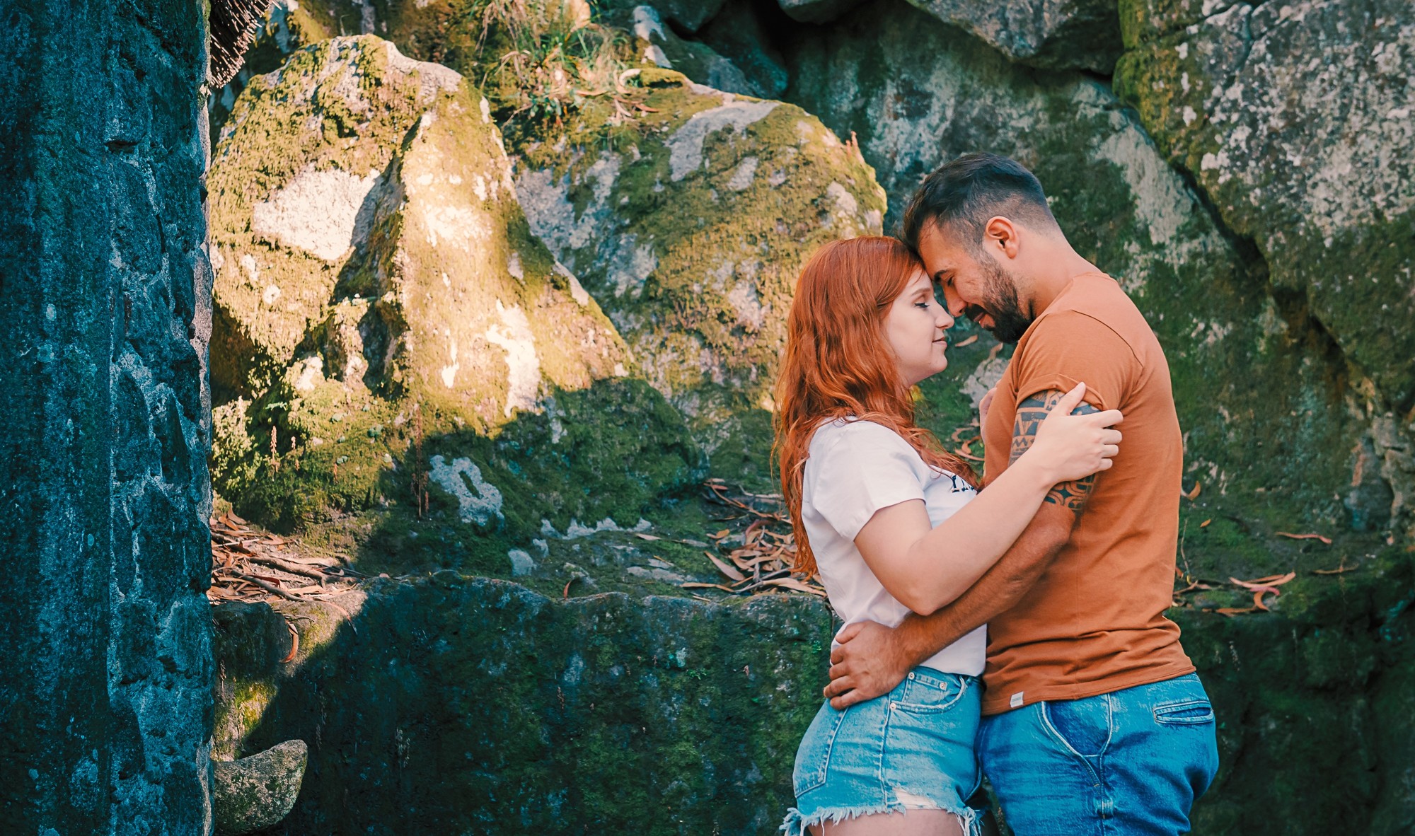 Casal a beira das rochas com as cabeças encostadas uma na outra