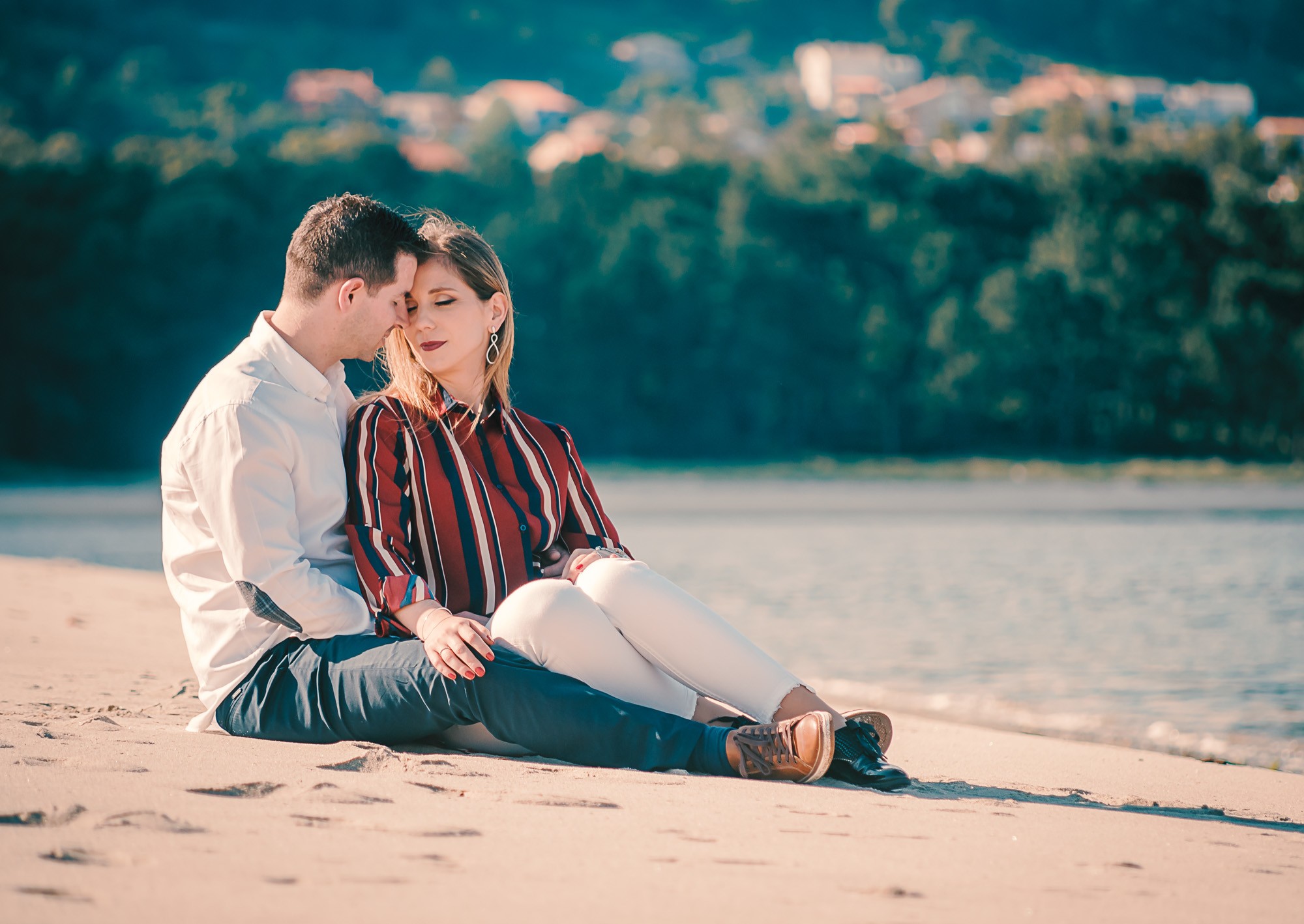 Casal com a cabeça encostada uma na outra sentados na areia