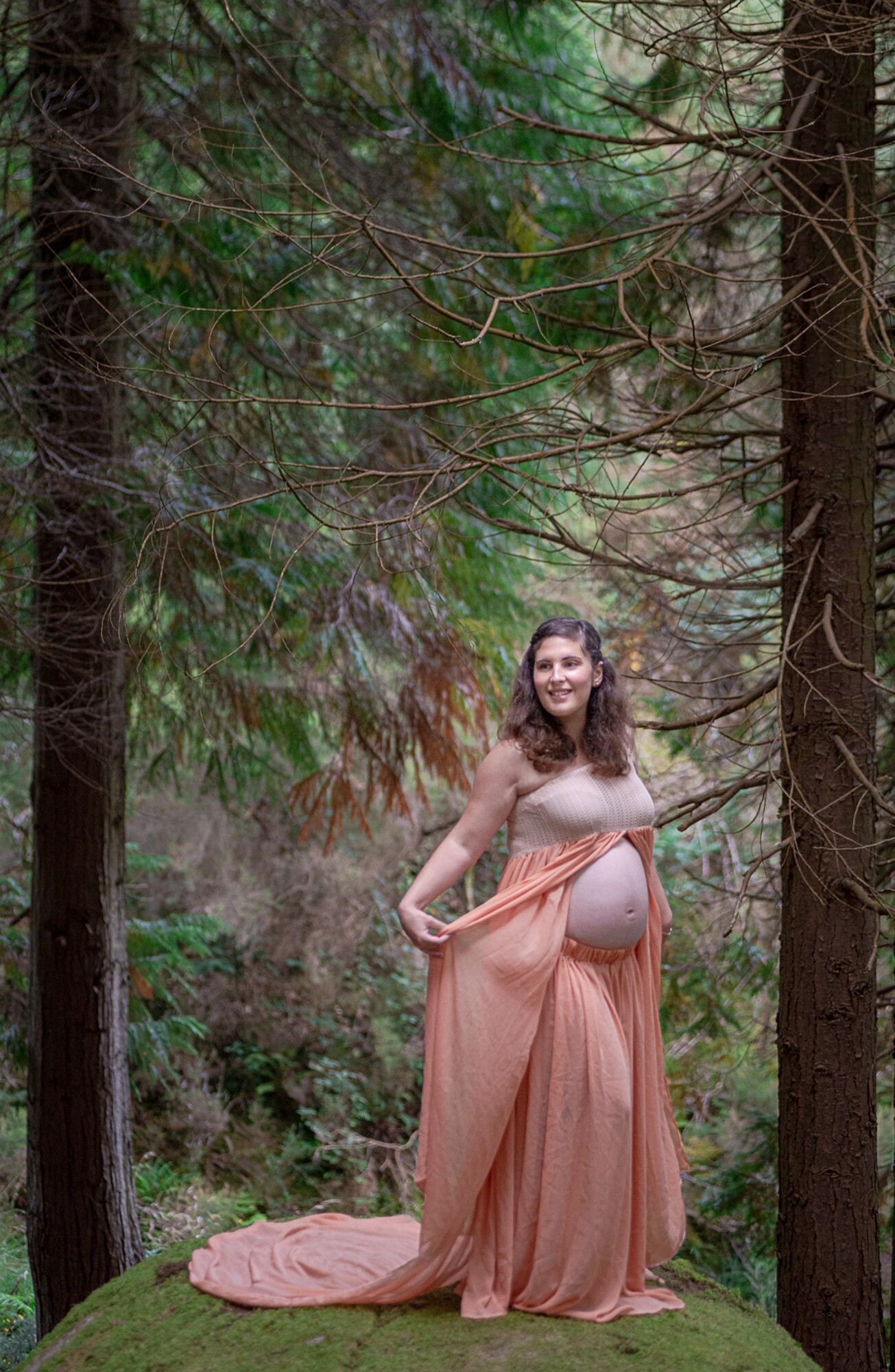 Pré-Mamã a segurar no vestido a sorrir no bosque