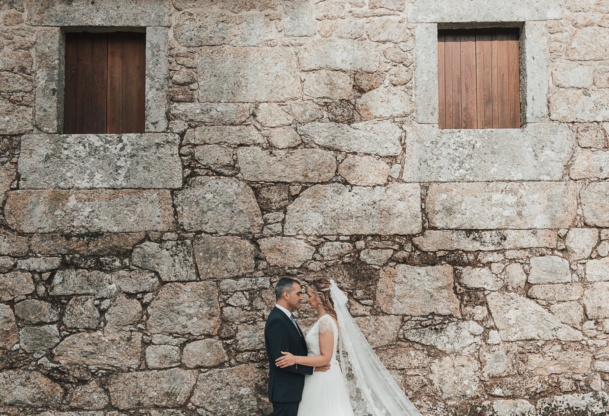 Casal a olharem um para o outro encostados a uma casa de pedra