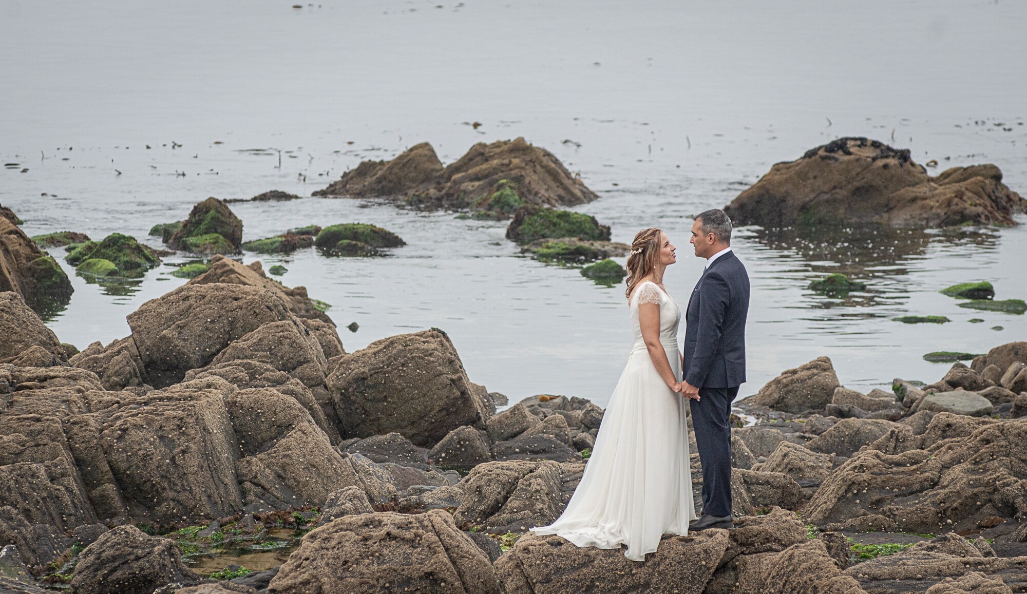 Casal em cima das rochas a olharem um para o outro a beira mar
