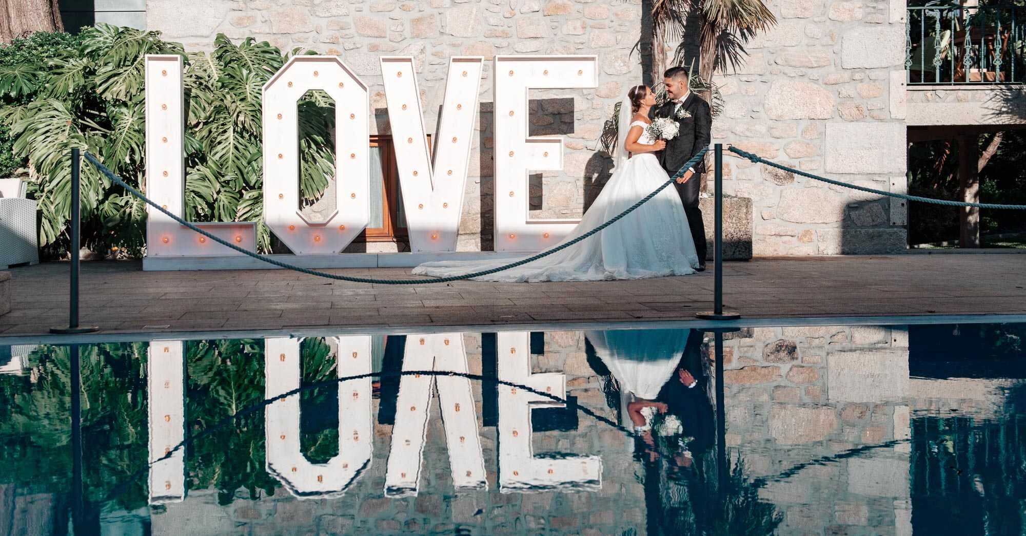 Casal a beira de um letreiro a dizer "LOVE"