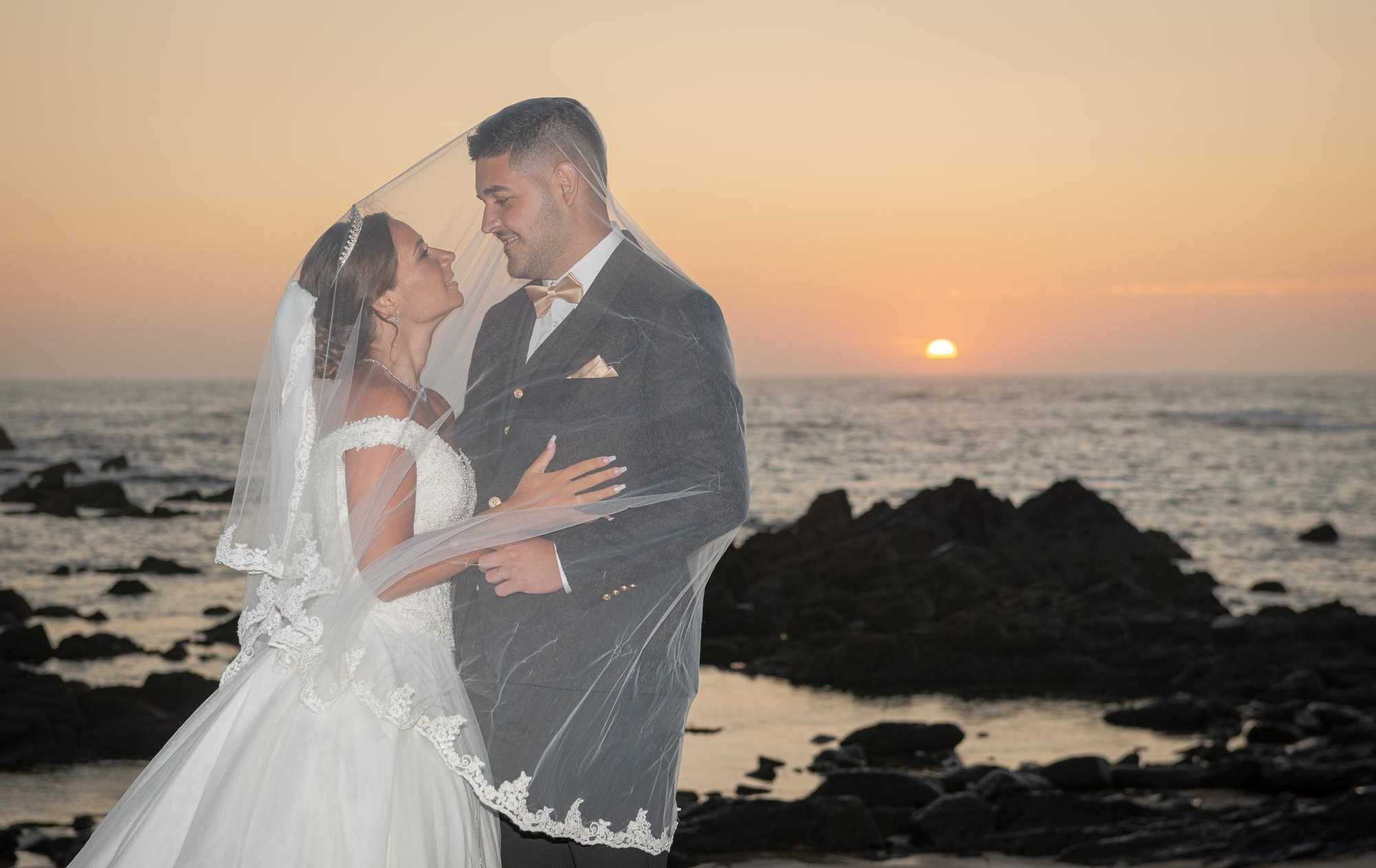 Casal dentro no véu da noiva na praia