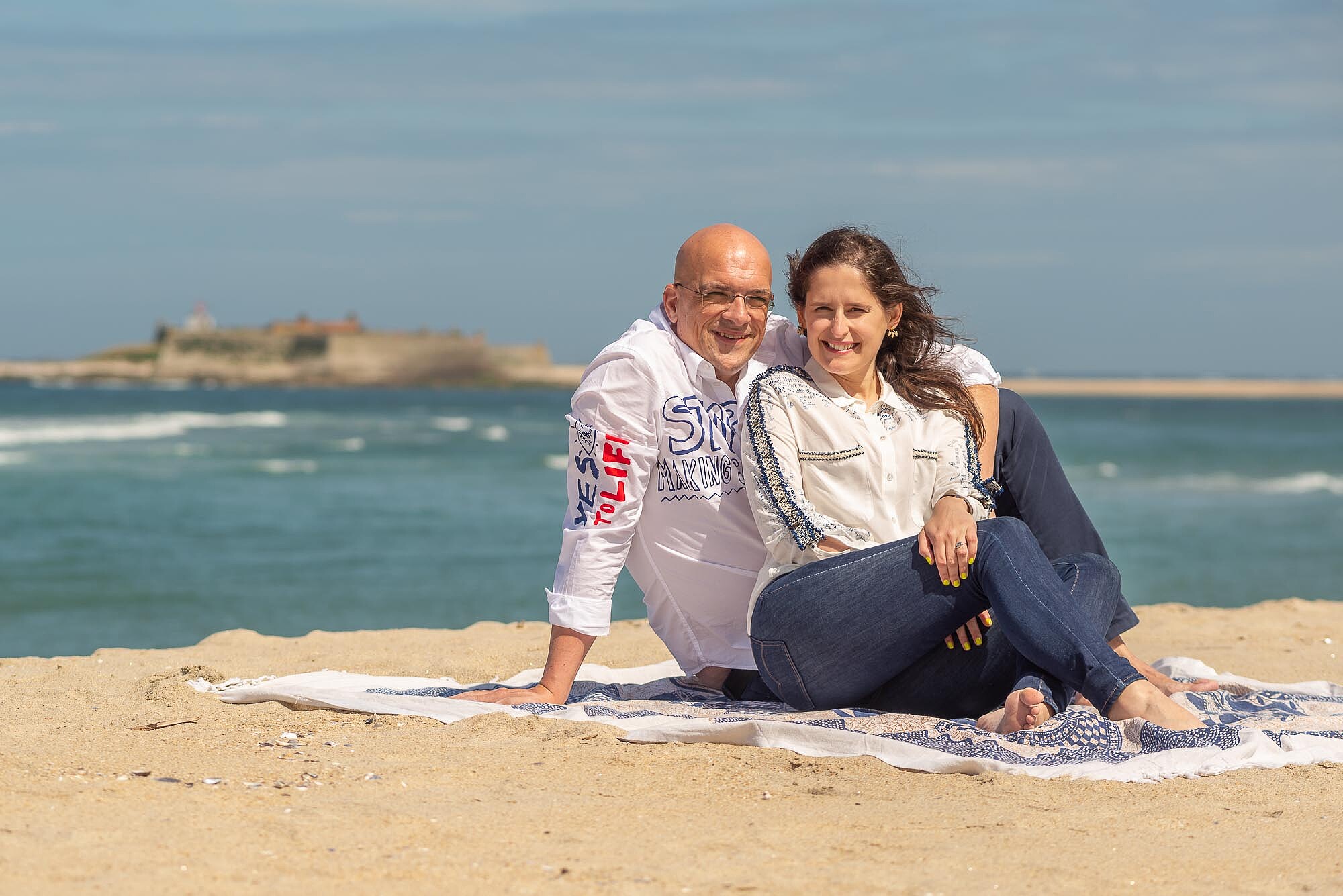 Noivos sentados numa toalha de praia a beira mar