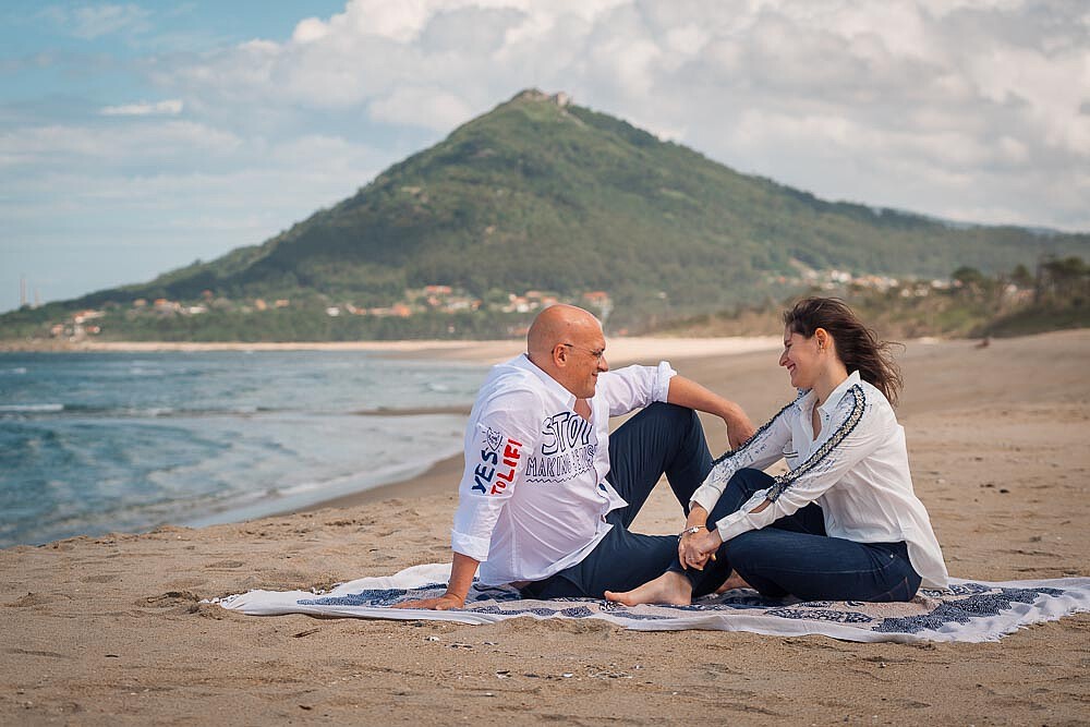Casal sentado na praia sentados numa toalha e a conversarem