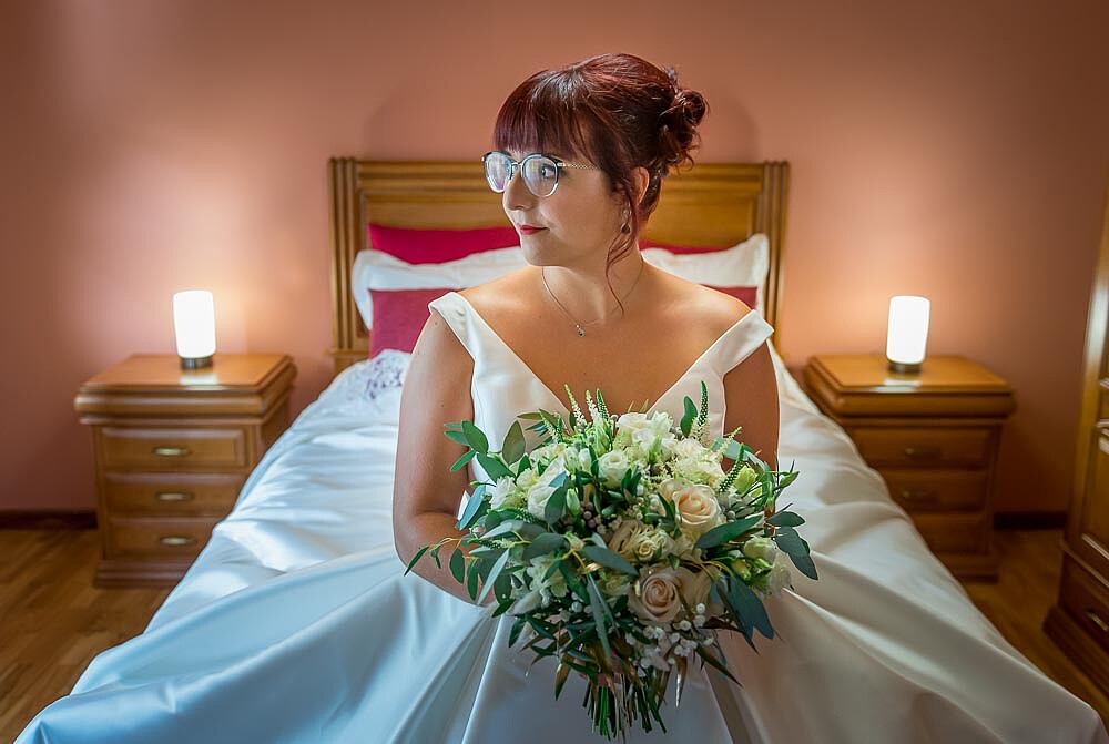 Noiva sentada na cama com o buque de flores