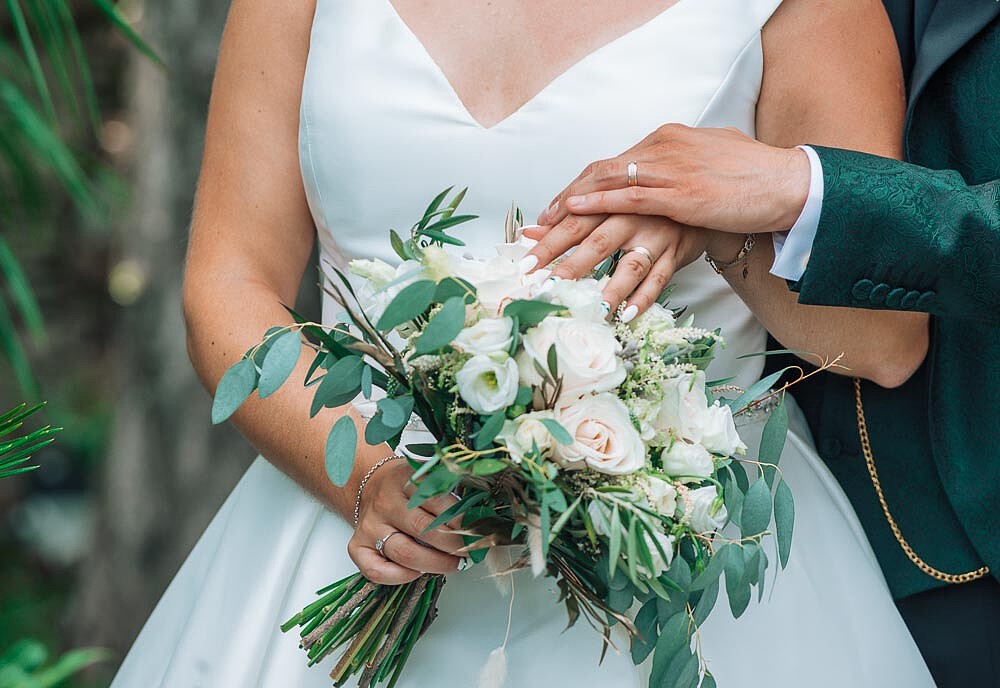 Pormenor do ramo das flores e das mãos dos noivos com as alianças