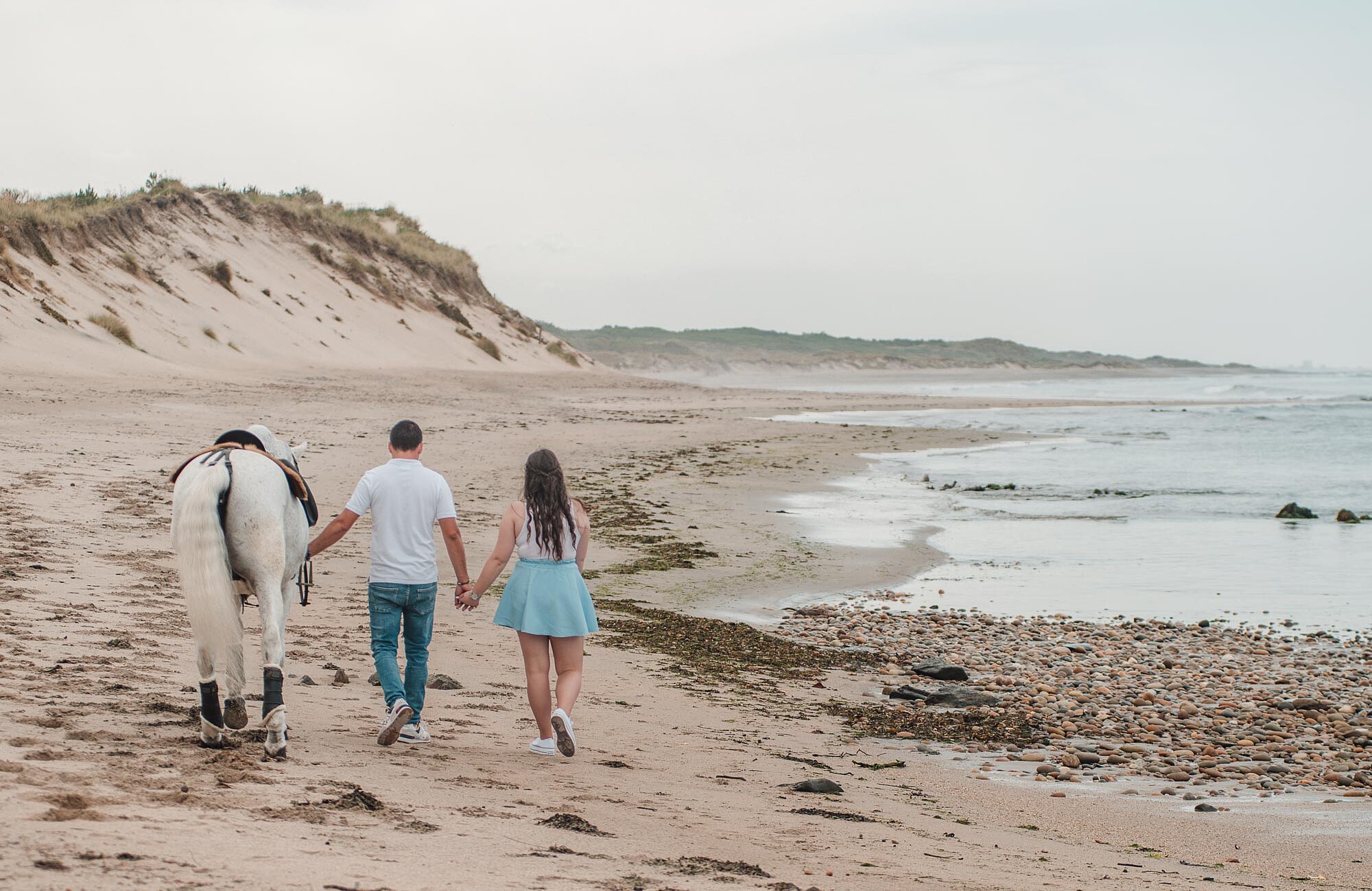Casal a caminhar com o cavalo na praia