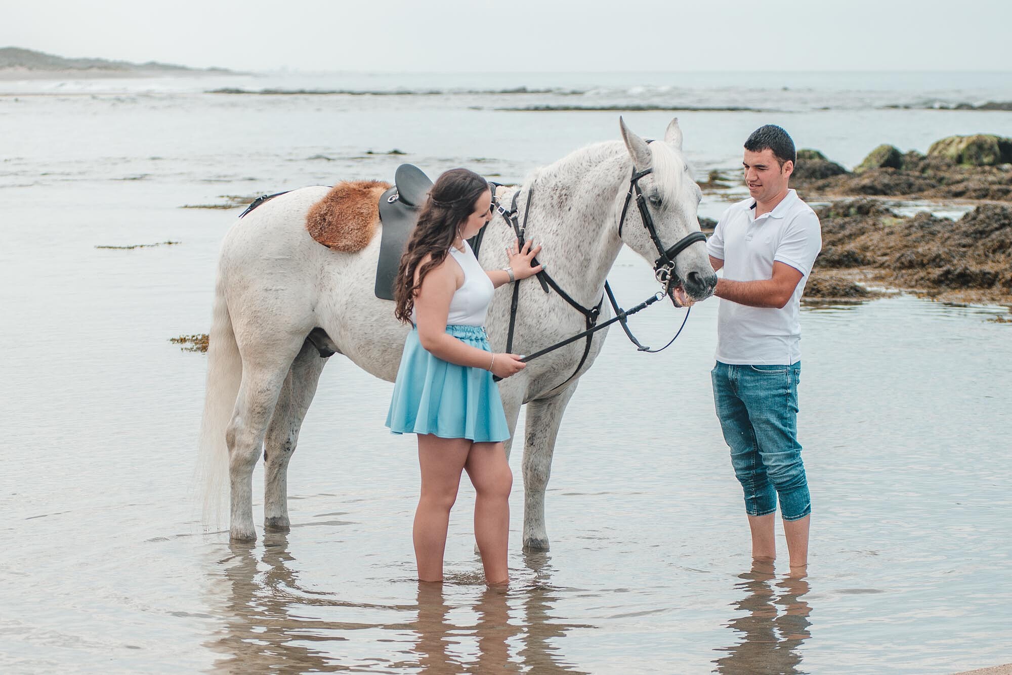 Casal dentro de &aacute;gua a fazer carinho no cavalo