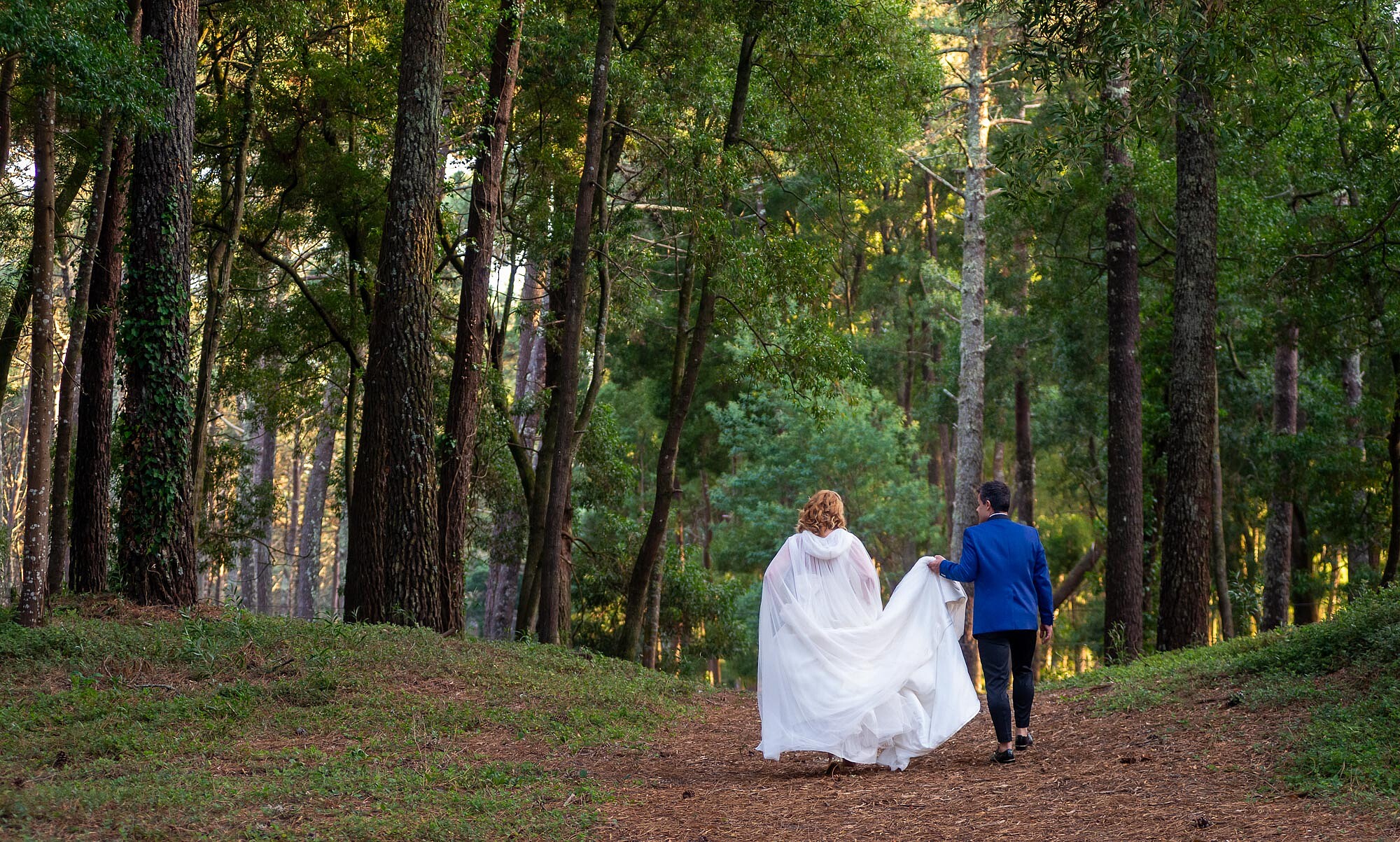 Homem a segurar o vestido da Noiva enquanto caminham pelo o bosque