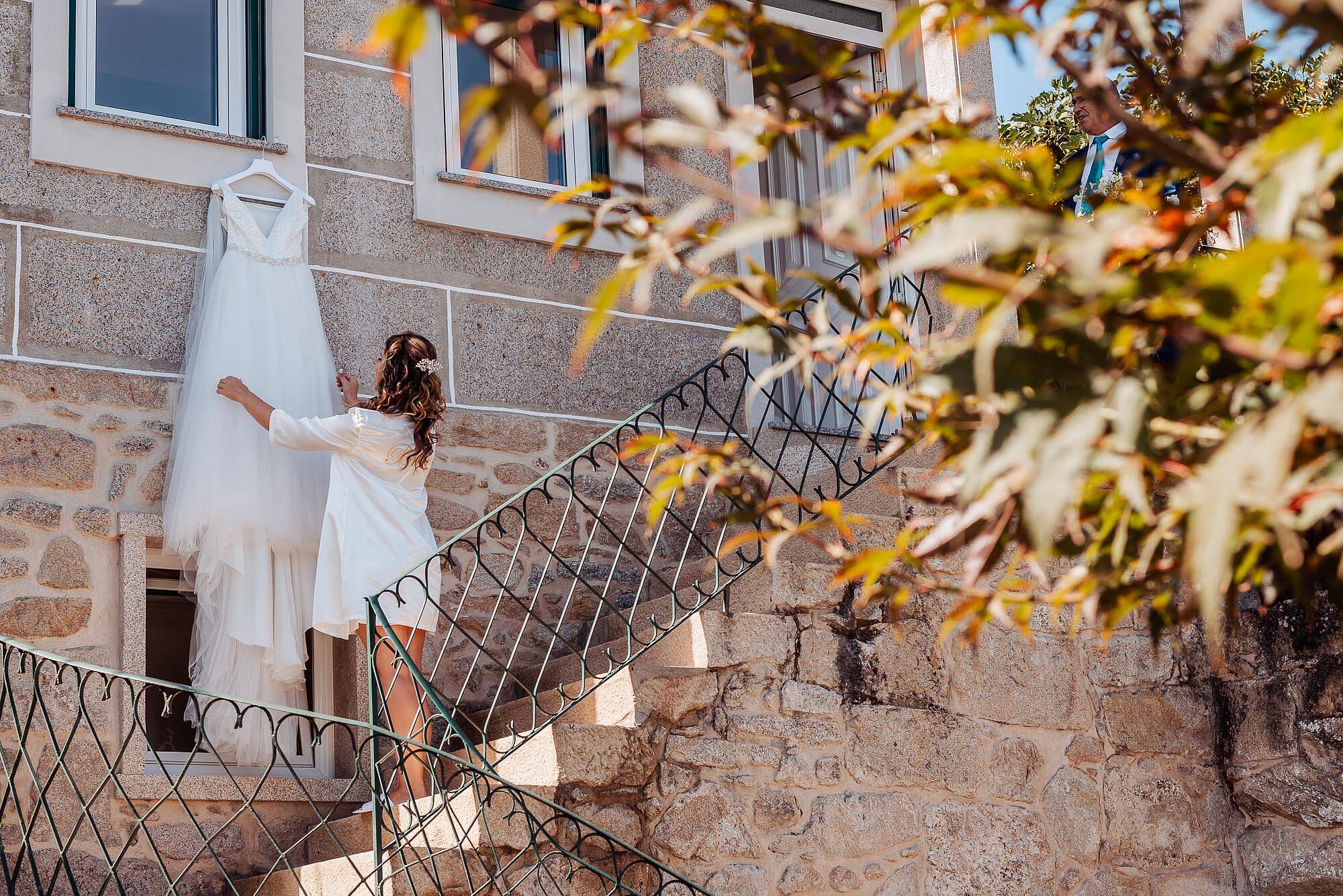 noiva a olhar vestido no seu dia de casamento nas escadas da casa