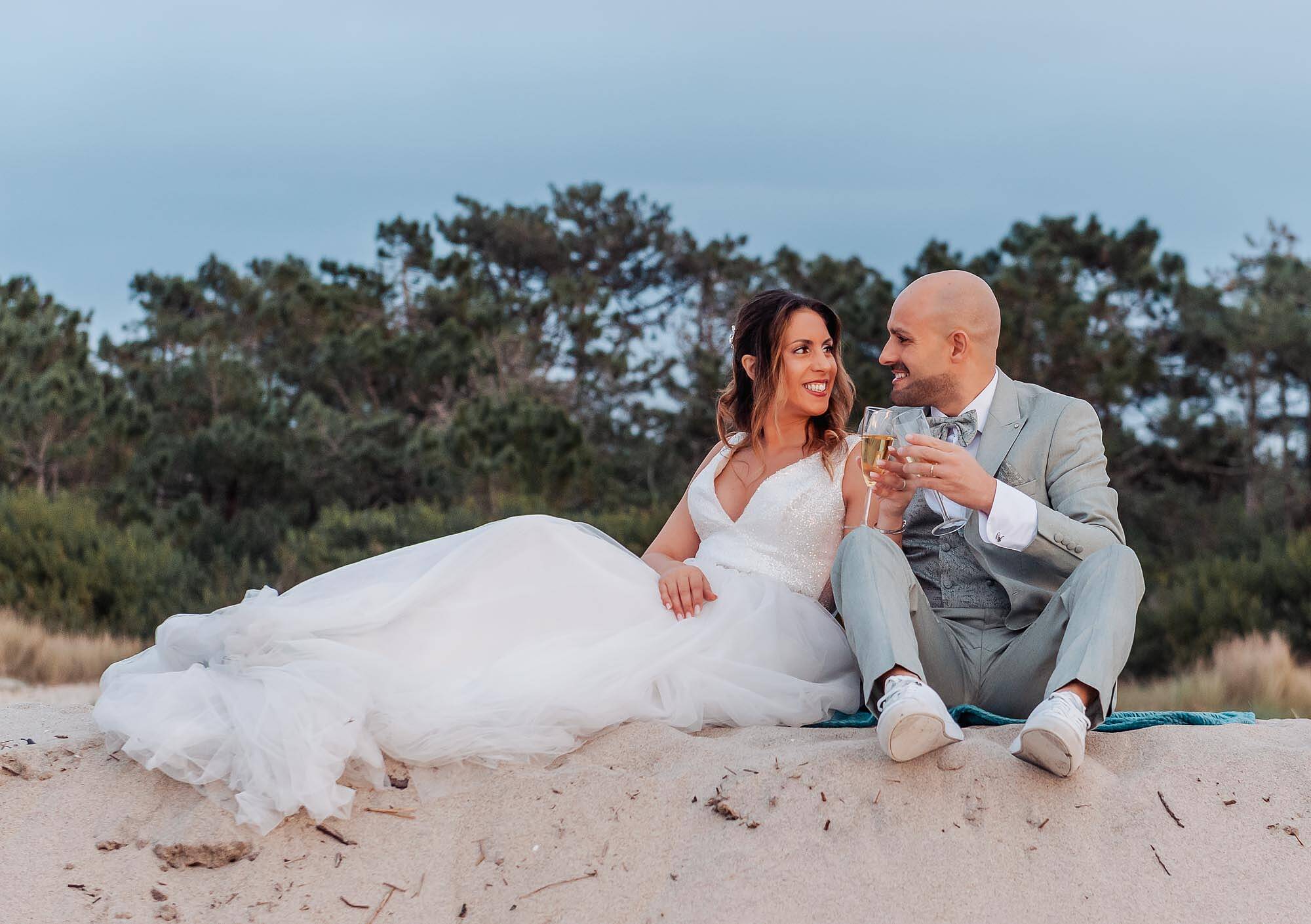 noivos sentados na areia a brindar