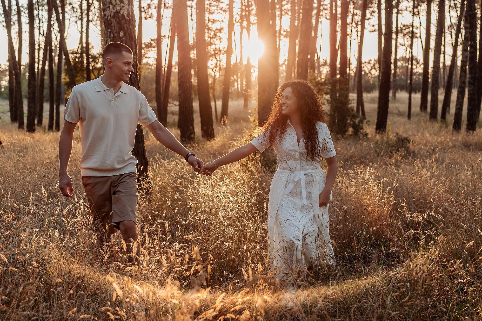 casal a caminhar de maos dadas no meio da floresta iluminada pelo sol