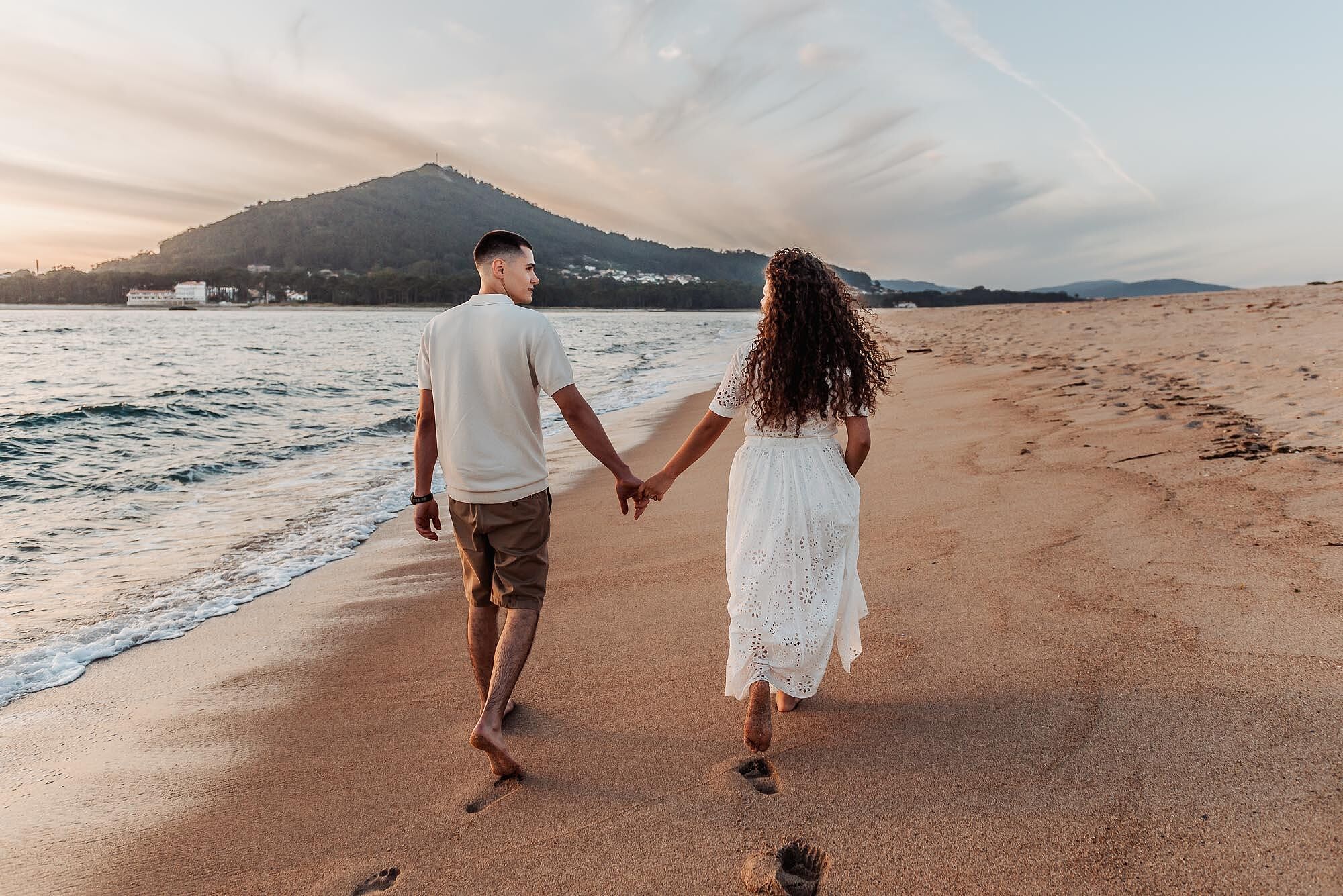 casal a caminhar de maos dadas pela praia deixando pegadas na areia