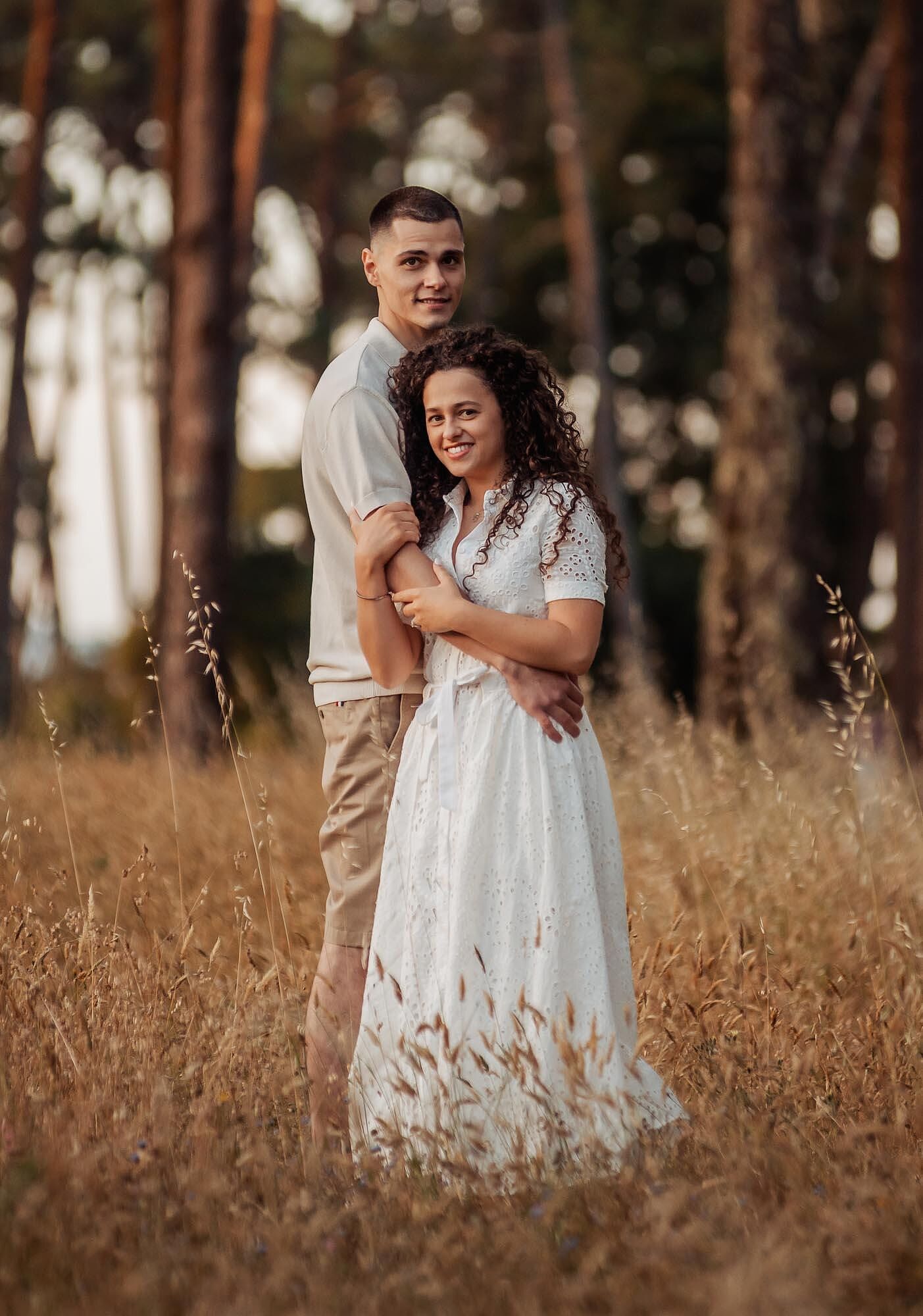 casal abracado de pe no campo com arvores ao fundo