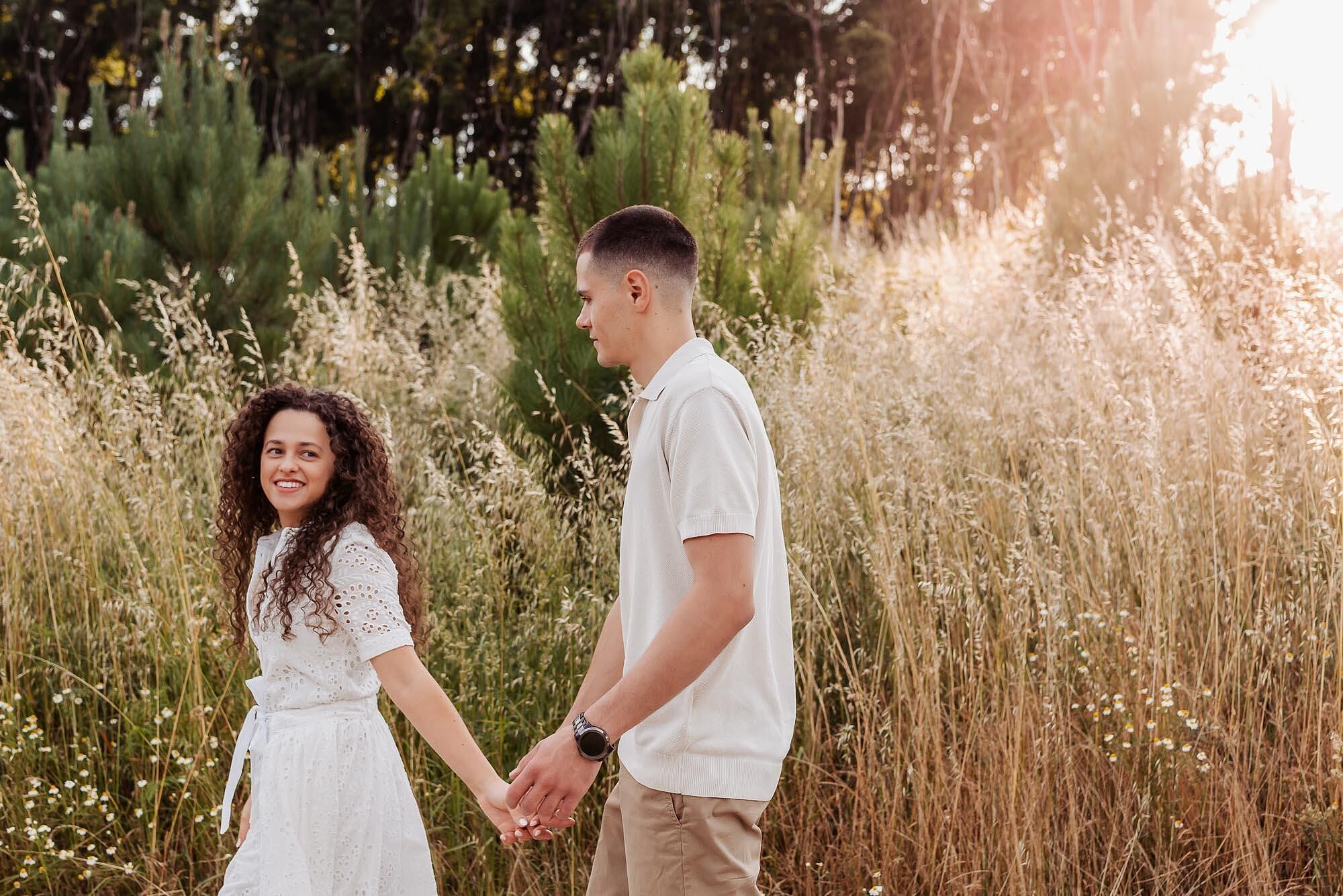 casal de maos dadas a caminhar junto a campo de ervas ao pôr do sol