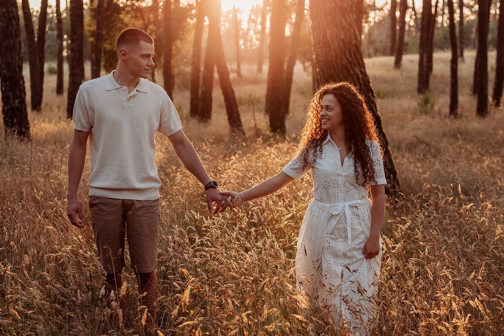 casal de maos dadas a sorrir no meio da floresta ao pôr do sol