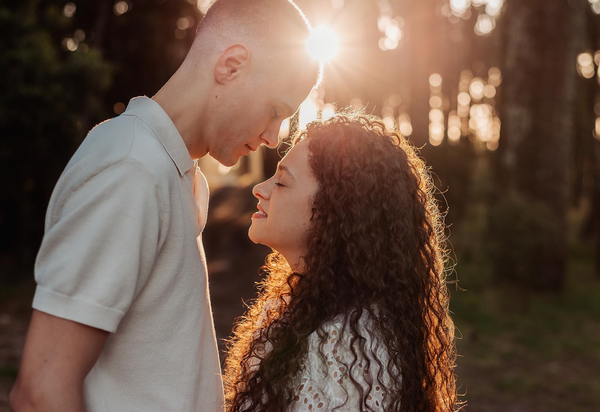 casal frente a frente com sol a brilhar entre as arvores