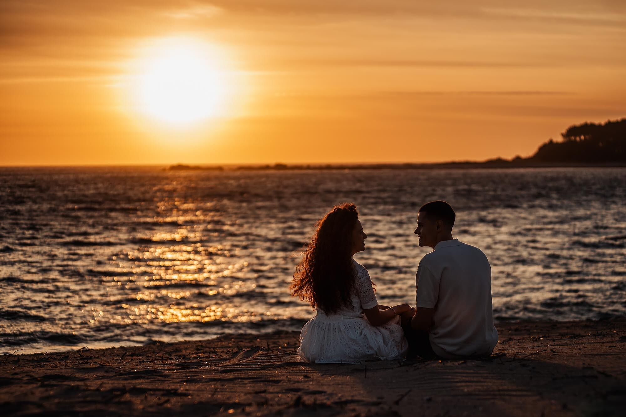 casal sentado frente ao mar a admirar o pôr do sol