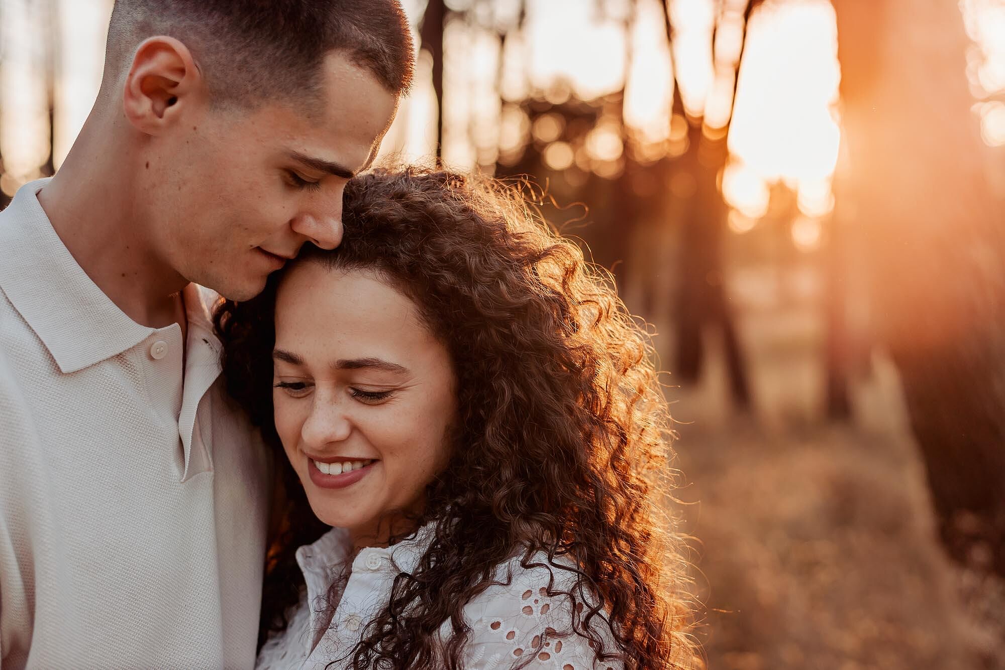 homem beija a testa da mulher enquanto ela sorri em cumplicidade