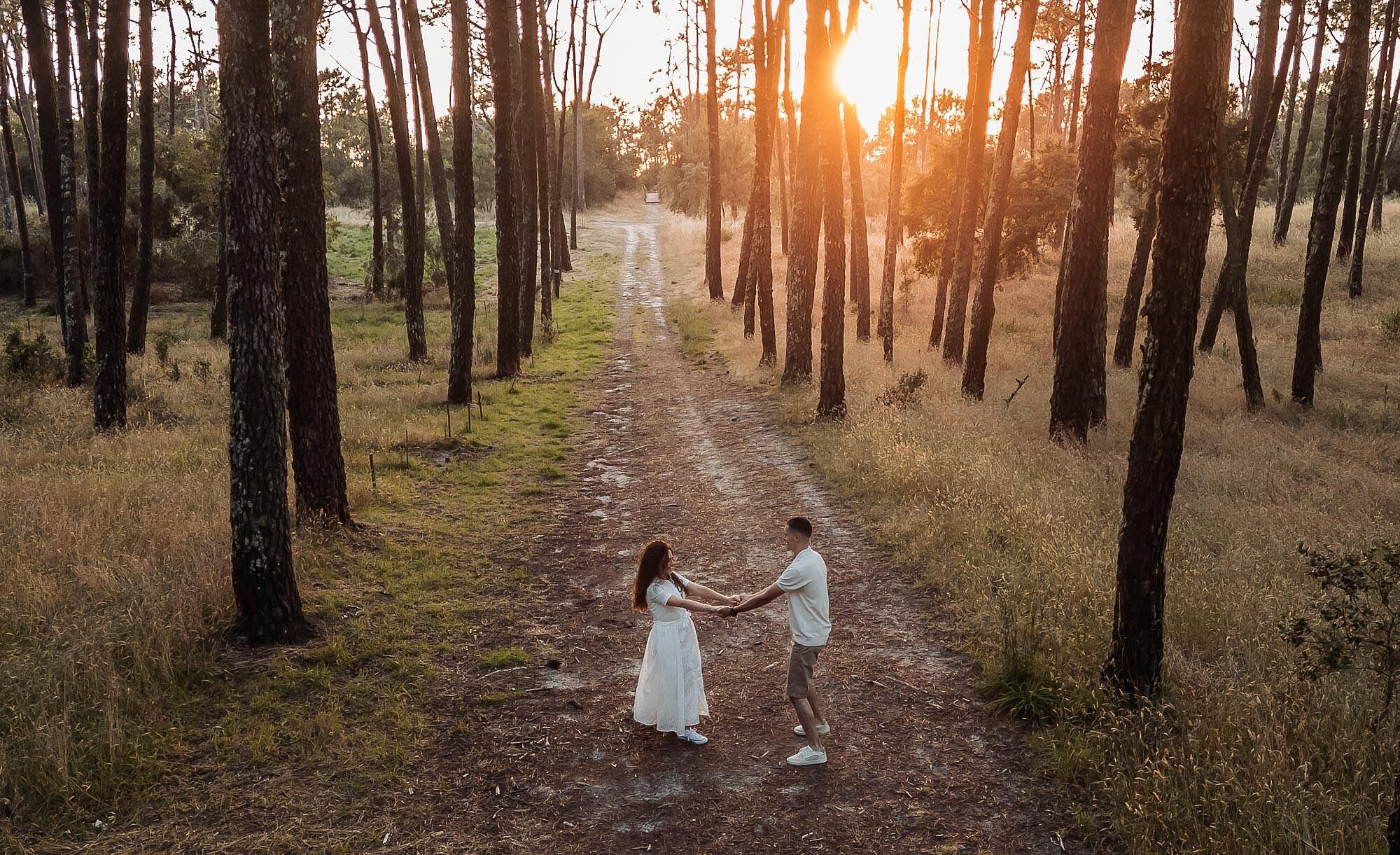 vista aerea de casal de maos dadas no meio de caminho na floresta ao pôr do sol