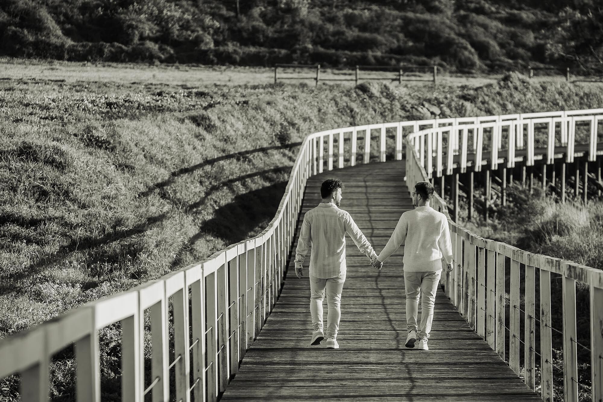 foto a preto e branco de casal a caminhar em passadiços junto á praia