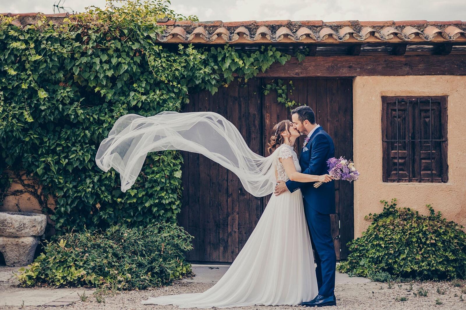 Novios besándose en boda rústica en Castilla y León con velo al viento