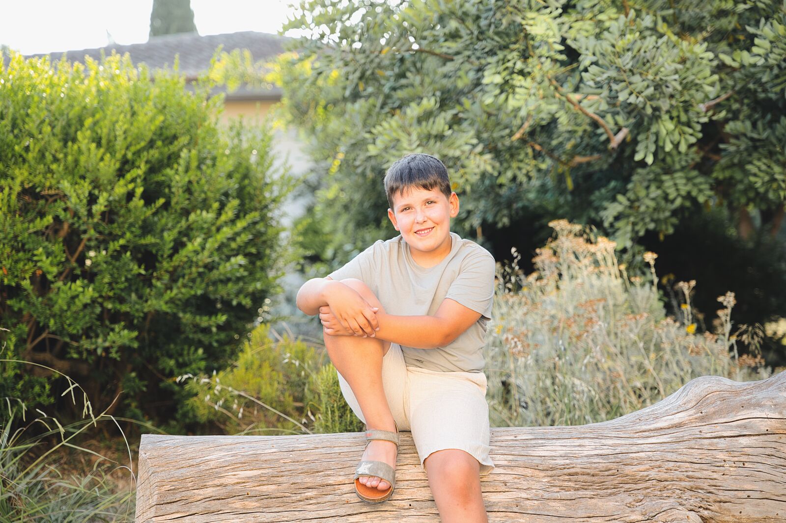 Niño sonriente sentado sobre un tronco rodeado de vegetación en L’Estany de l’Ullal