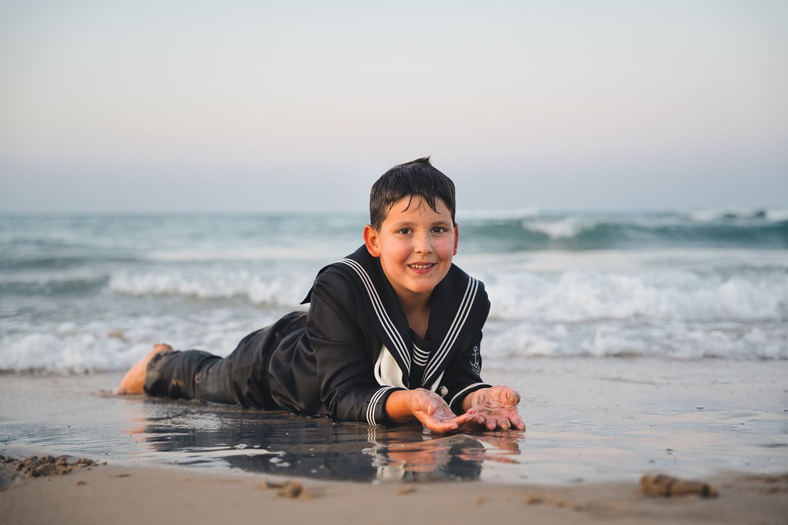 Niño acostado en la arena mojada junto al mar en la playa de Gandía