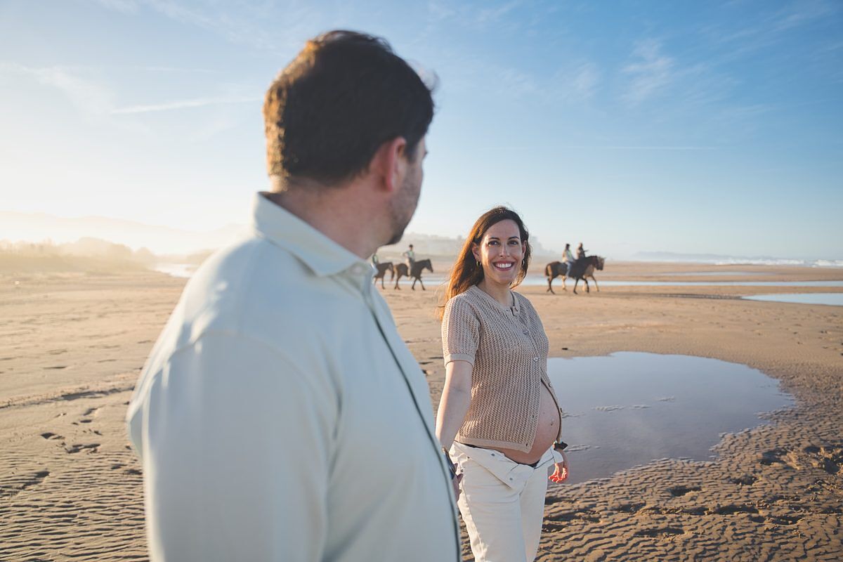 Futura mamá sonriendo en la playa de Xeraco con caballos al fondo - fotógrafo embarazo Xeraco Gandía