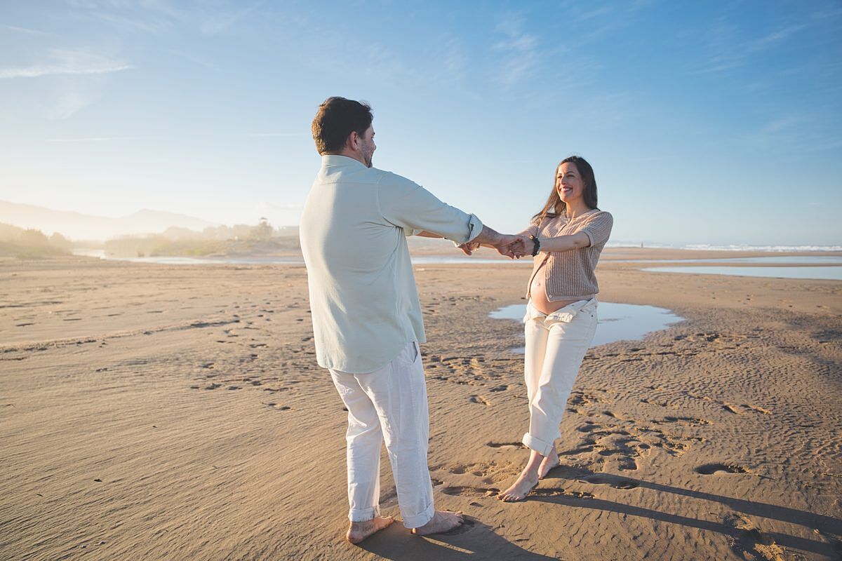 Pareja bailando cogidos de las manos en la playa de Xeraco - sesión embarazo fotógrafo Juan Reig