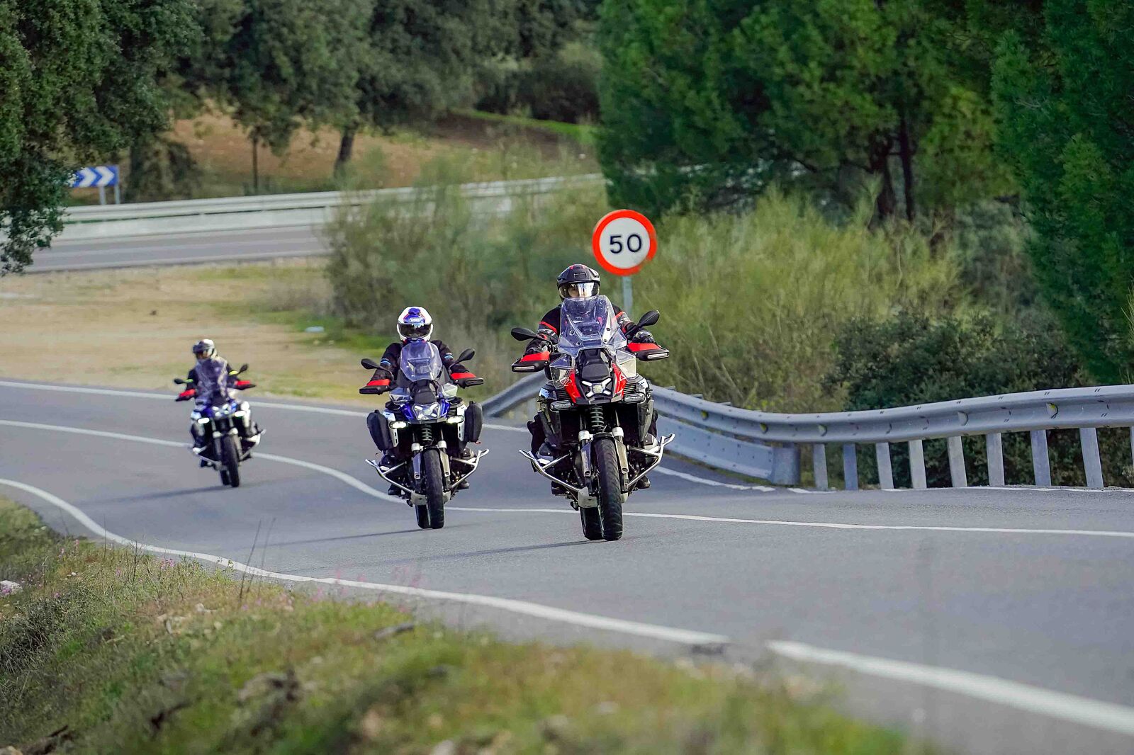 Tres motocicletas tipo Maxitrail BMW GS rodando en grupo por una curva de la carretera AV-562 en Cebreros, Ávila, durante una sesión de fotografía de acción de Odinfoto.
