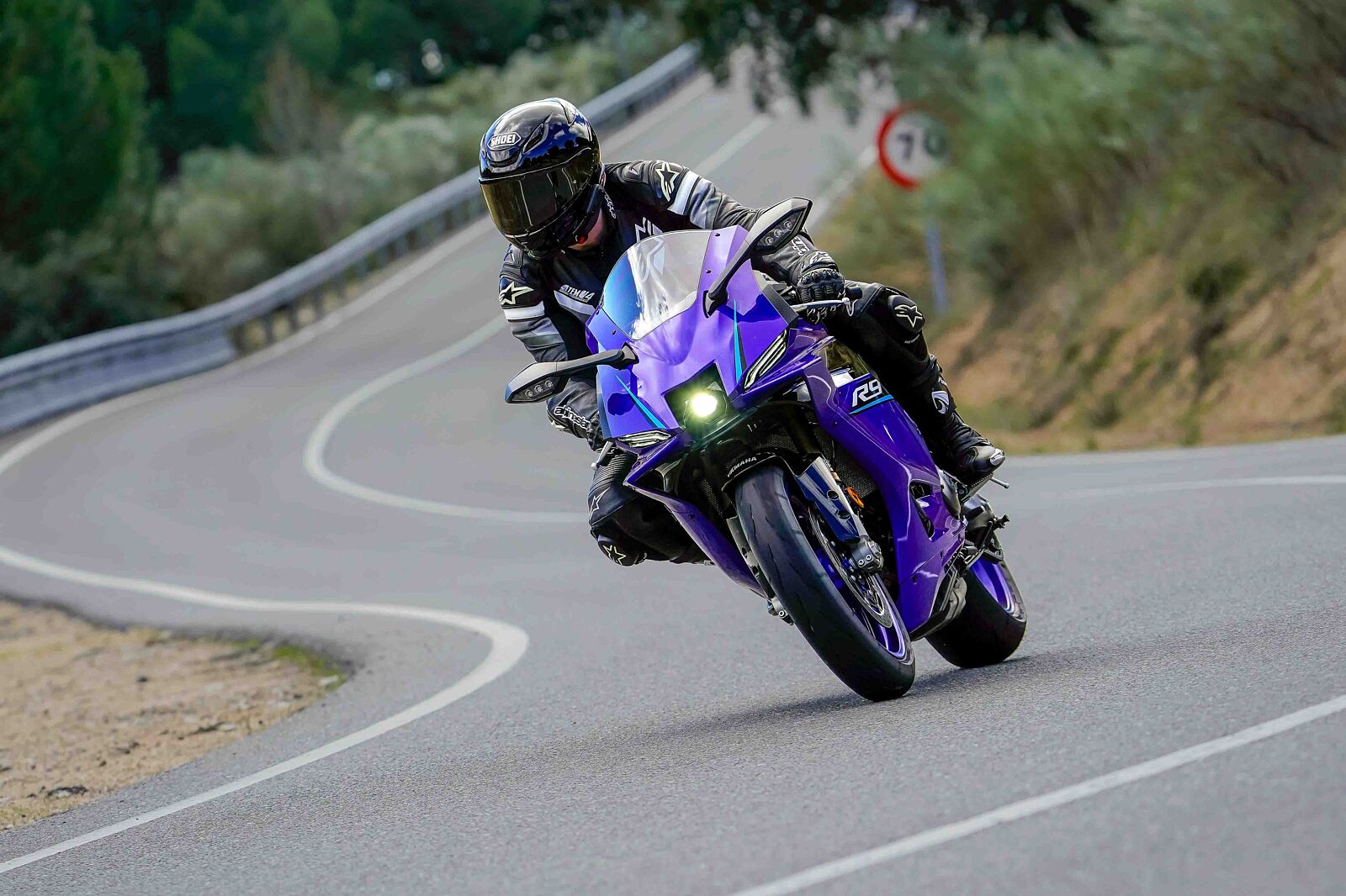 Piloto con equipación de cuero inclinando una moto deportiva Yamaha R9 azul al trazar la Curva Tamayo en la carretera AV-562, Cebreros, capturado en alta velocidad por Odinfoto.