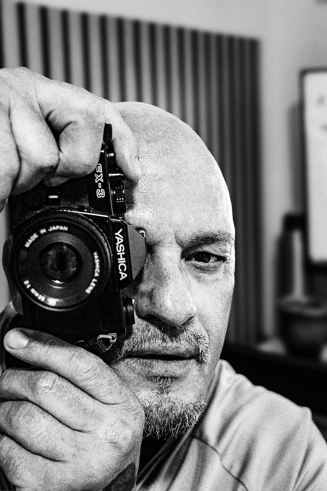 Retrato en blanco y negro del fotógrafo mirando a través del visor de una cámara analógica Yashica FX-3.