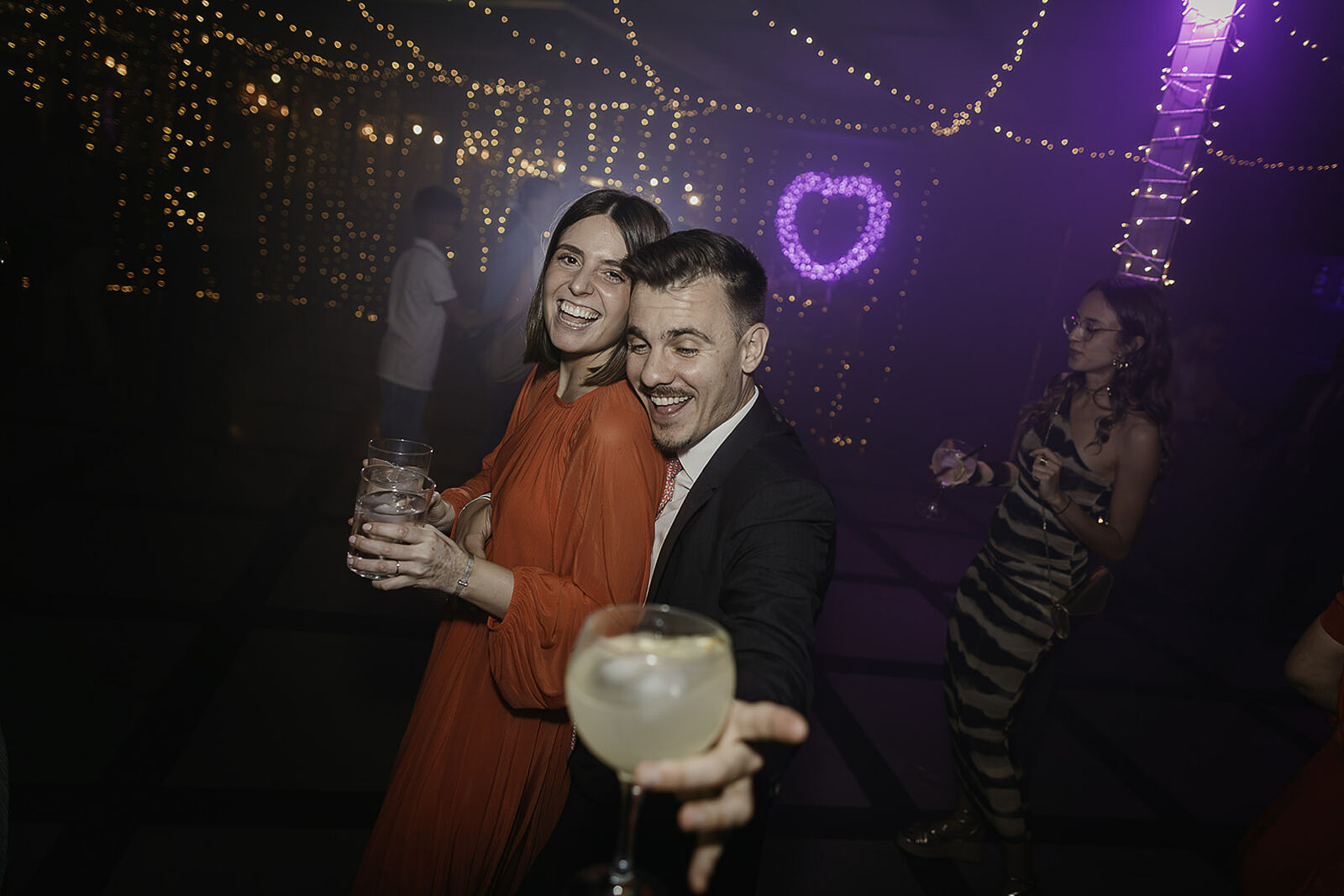 Pareja sonriendo y brindando en la fiesta de una boda en Madrid, capturada por Luzdesi Fotografía.