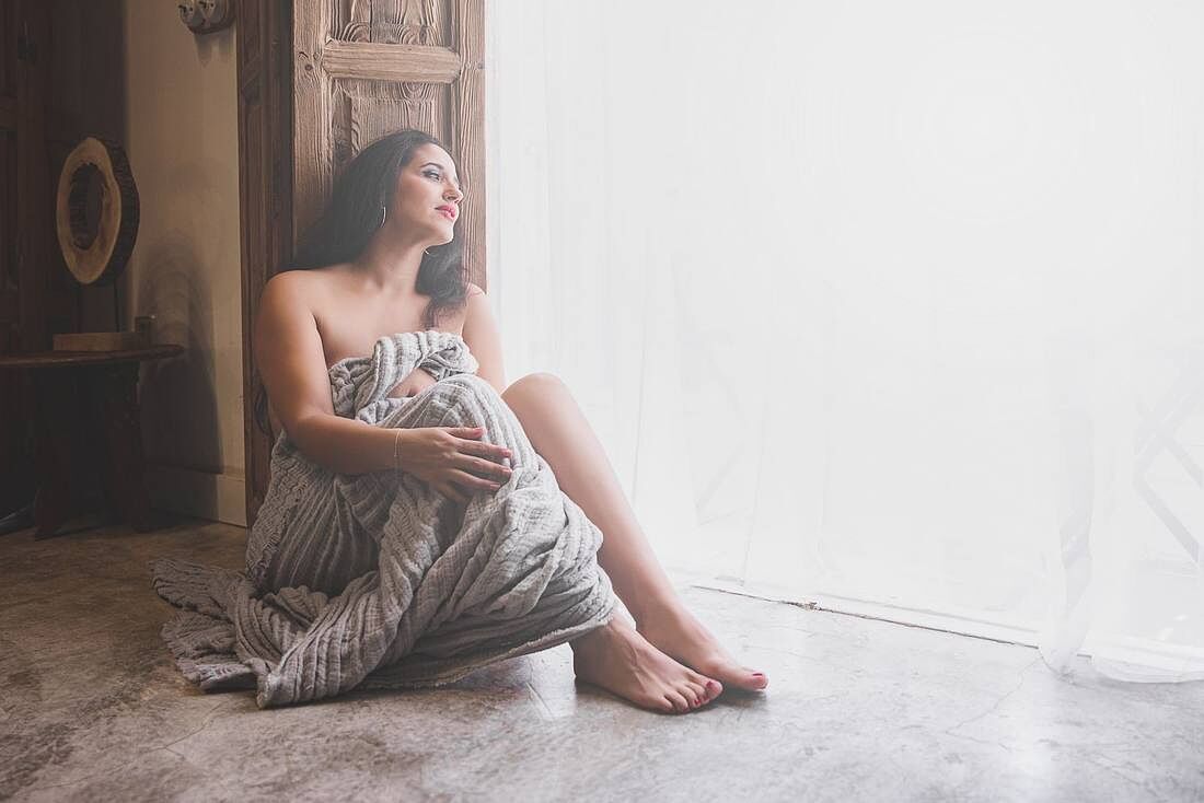 Mujer envuelta en tela junto a un gran ventanal de luz natural